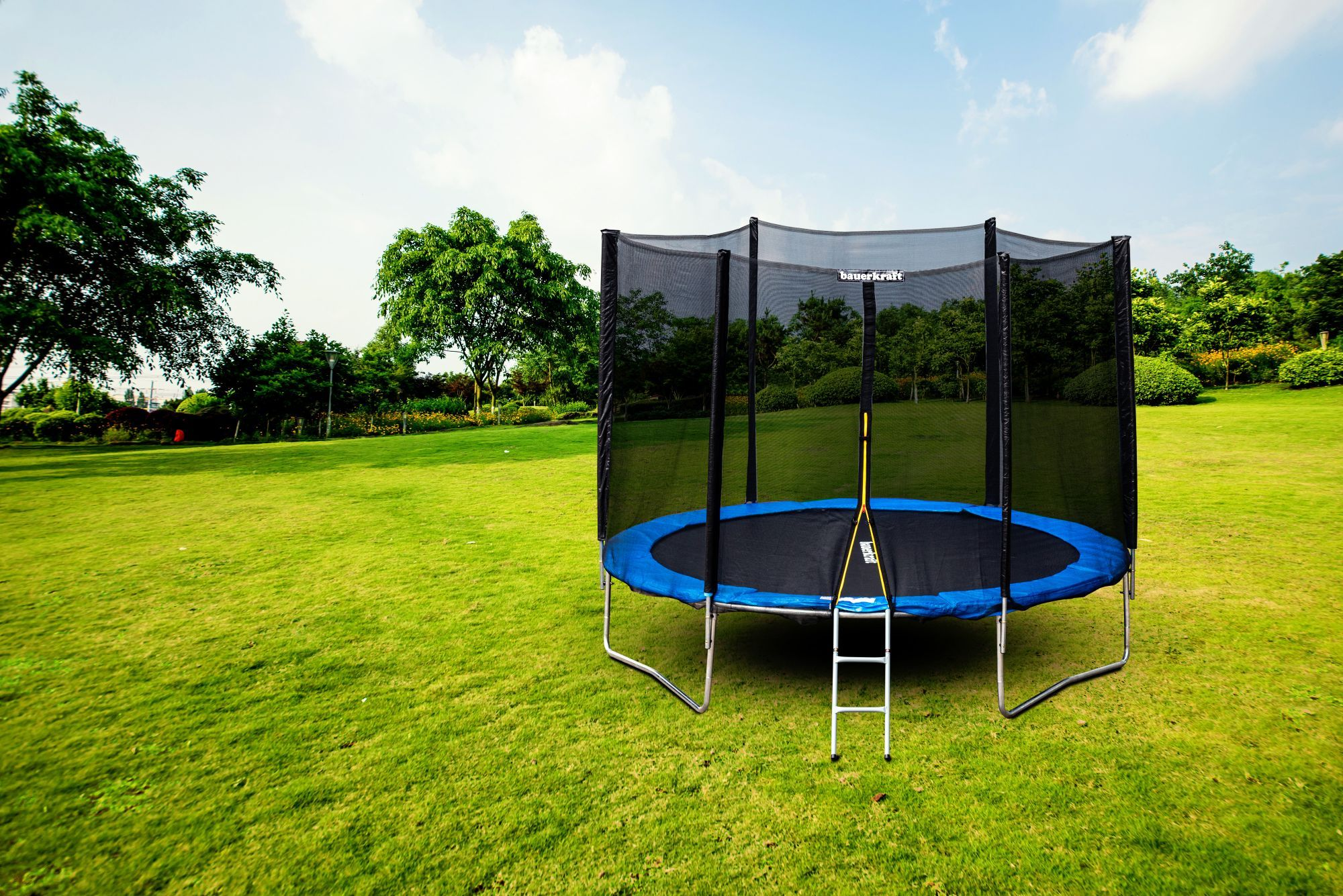 Trampolina z siatką zabezpieczającą i drabiną stoi na zielonym trawniku.