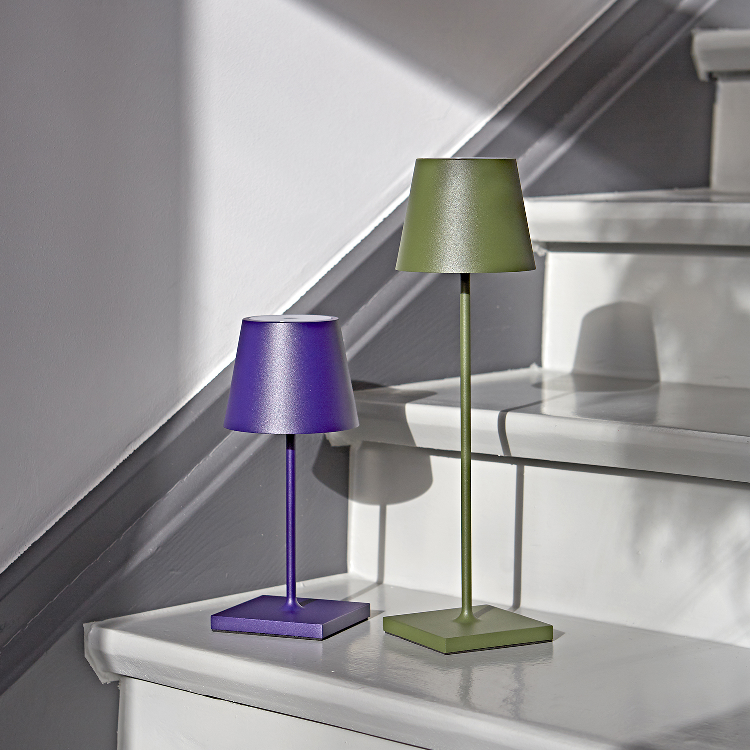 Zwei kleine Lampen, eine lila, eine grüne, stehen auf einer Treppe.
