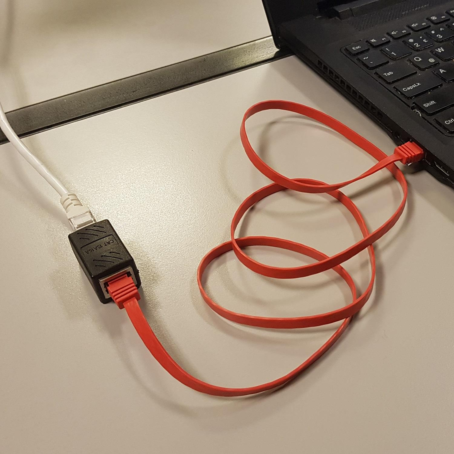 Kırmızı Ethernet kablosu bir dizüstü bilgisayarı siyah bir adaptöre ve beyaz kabloya bağlar.