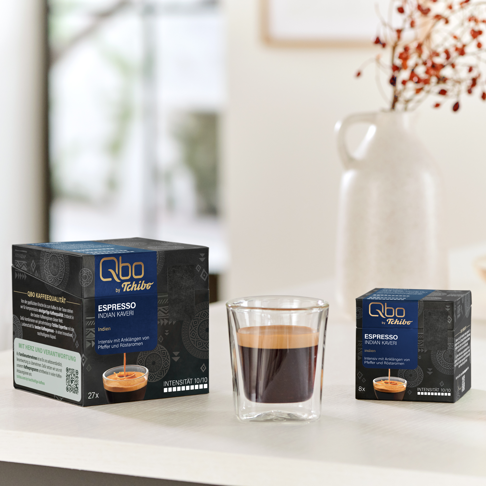 Zwei Packungen Qbo Espresso Indian Kaveri neben einem Glas Espresso.