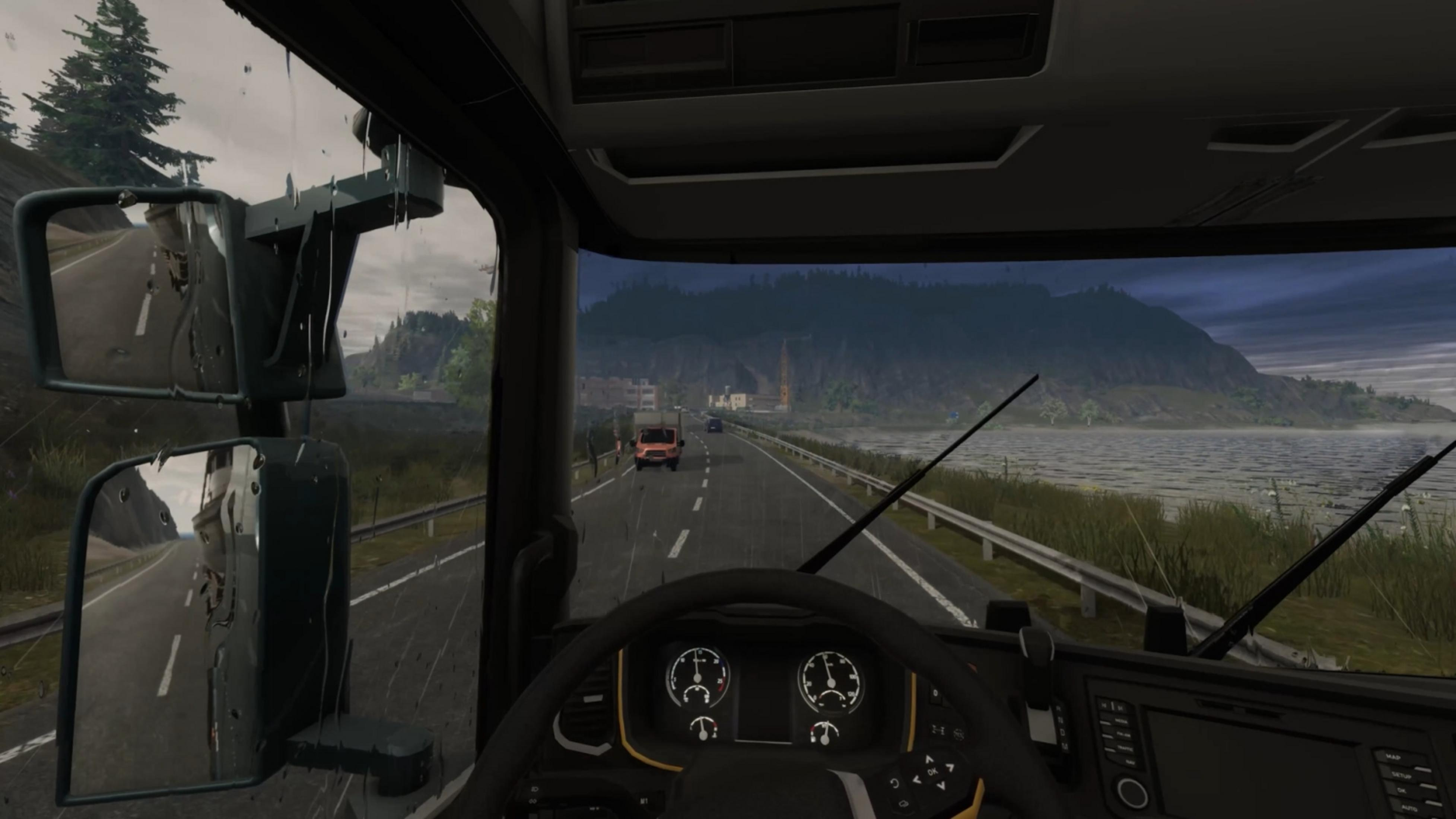 Blick aus einem LKW-Führerhaus auf eine nasse Straße mit Bergen und einem See.