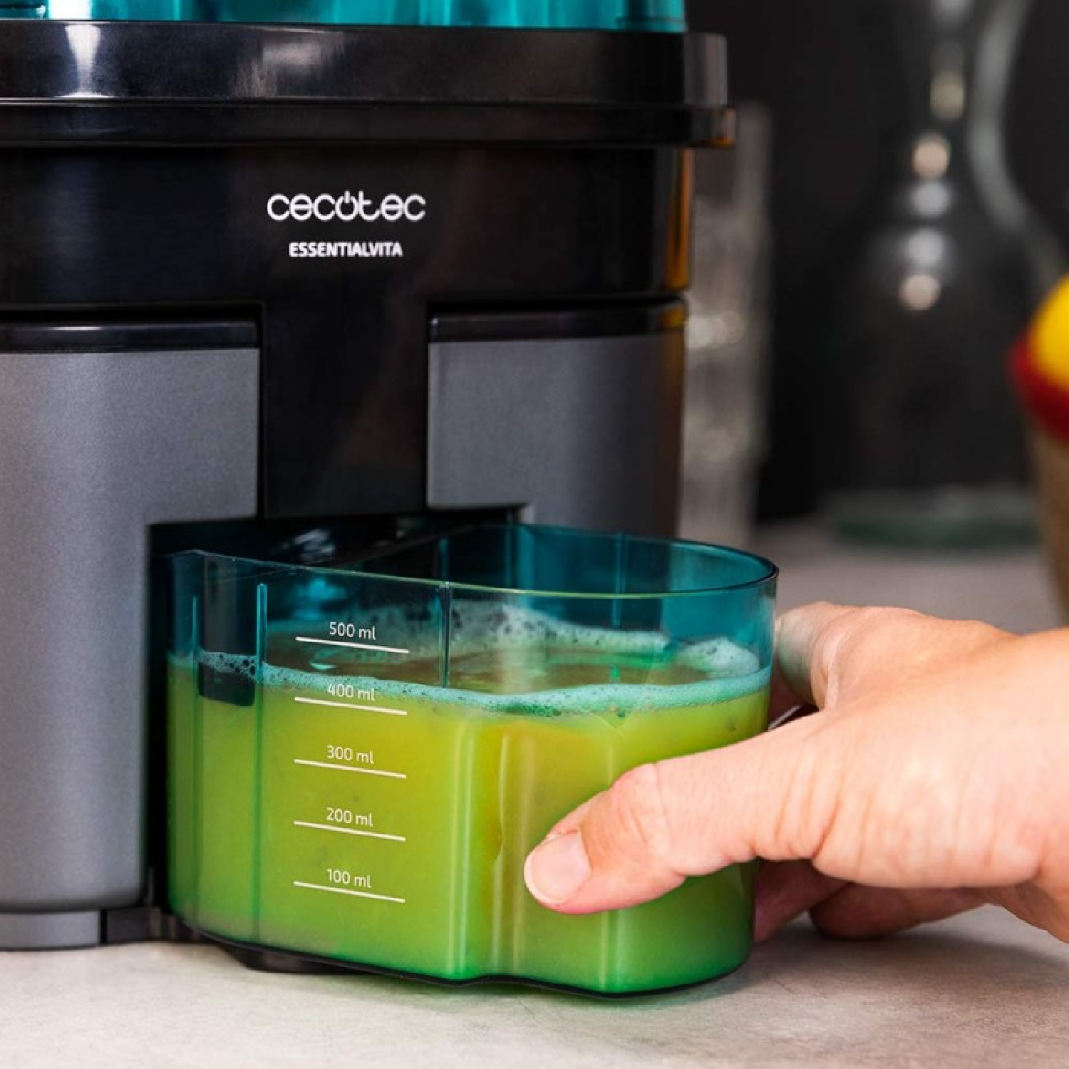 Mano rimuove contenitore con succo verde dall'estrattore. Segni fino a 500 ml.