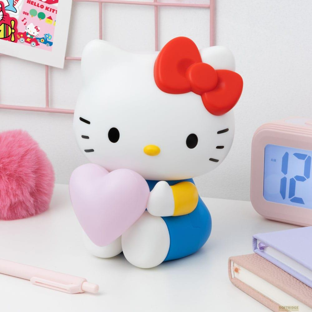 Figurka Hello Kitty trzyma różowe serce. Obok różowa kula, budzik i książki.