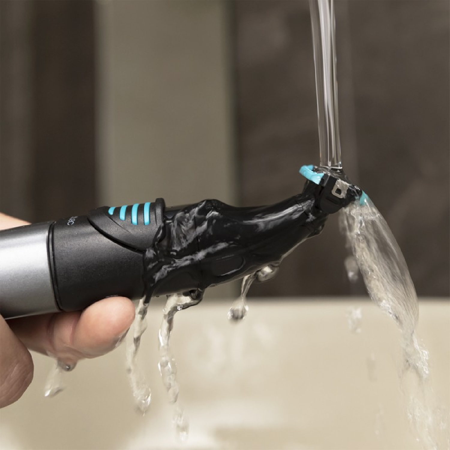 Un recortador negro se sostiene bajo agua corriente en un lavabo.