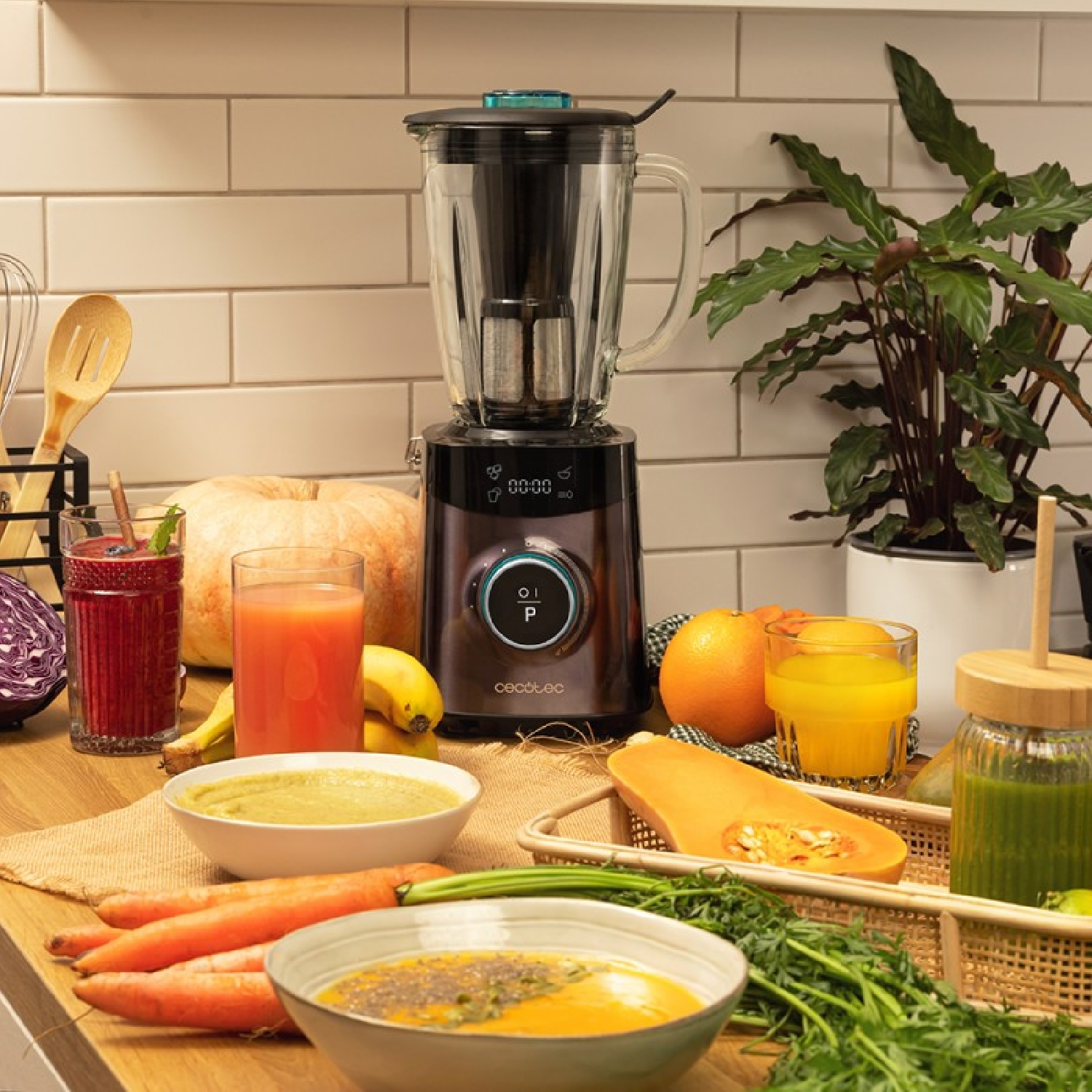 Blender stoi obok owoców i warzyw, takich jak marchew, dynia, pomarańcze i banany.