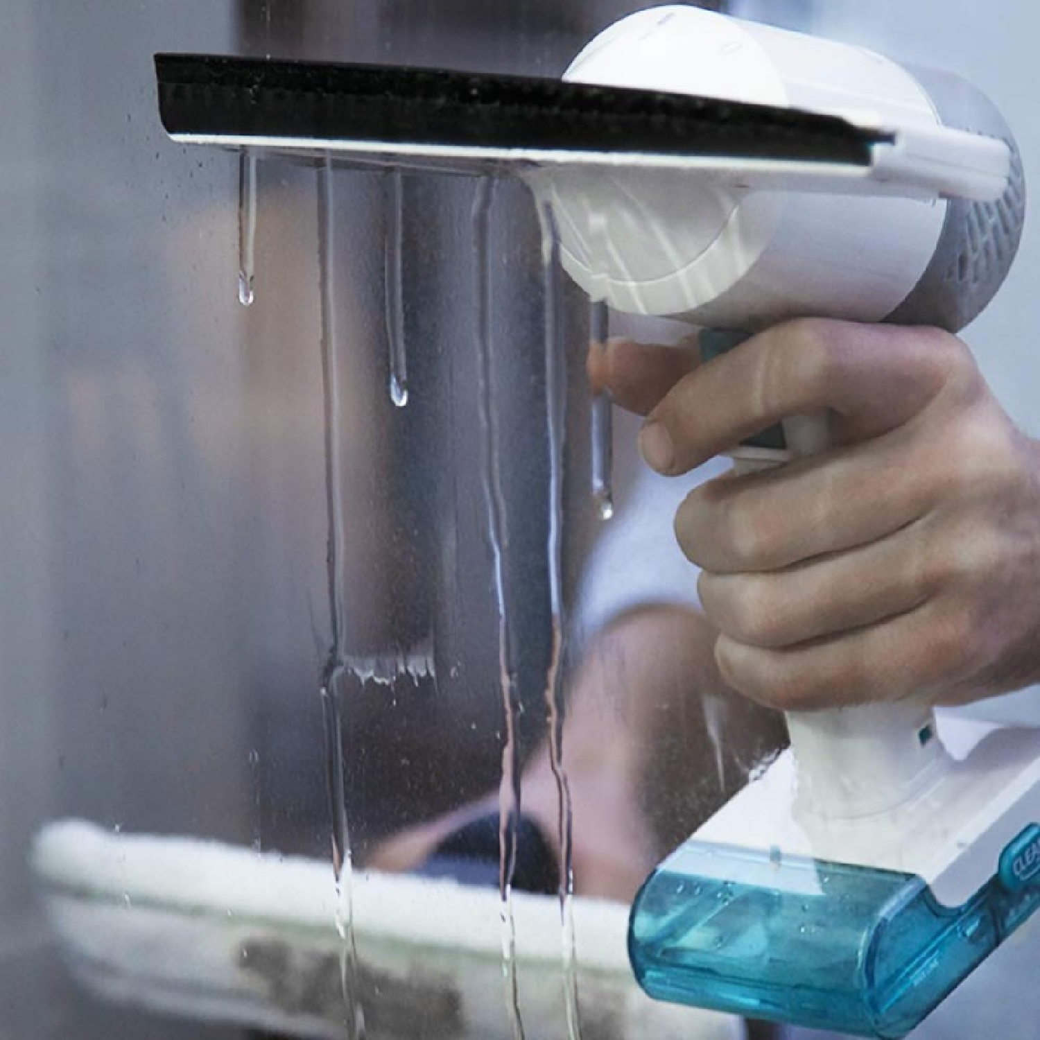 Hand hält Fensterreiniger, Wasser tropft von der Gummilippe auf Glas.