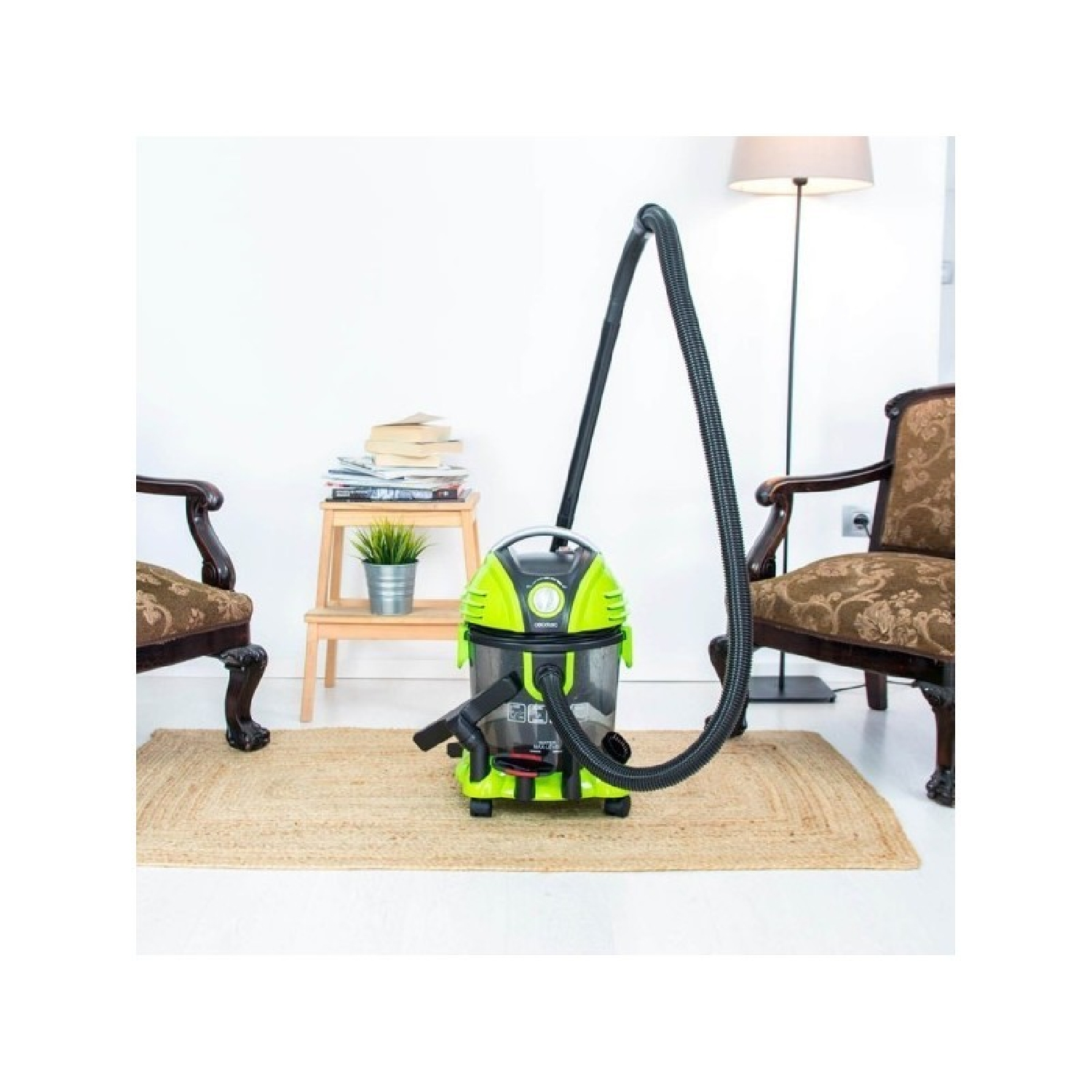 A green wet/dry vacuum cleaner sits on a rug between two armchairs.