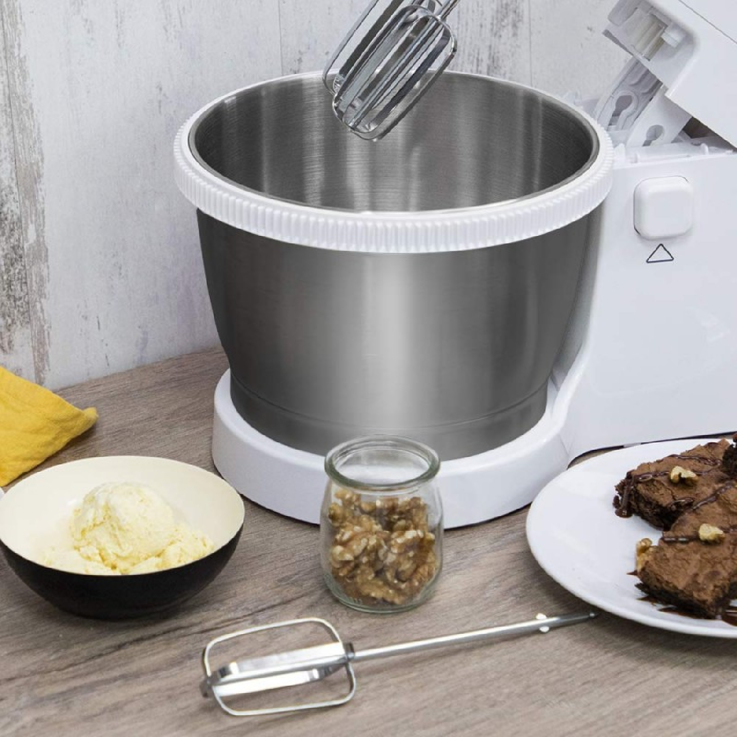 Ein Standmixer mit Schüssel, Eis, Brownies und Walnüssen auf einem Holztisch.