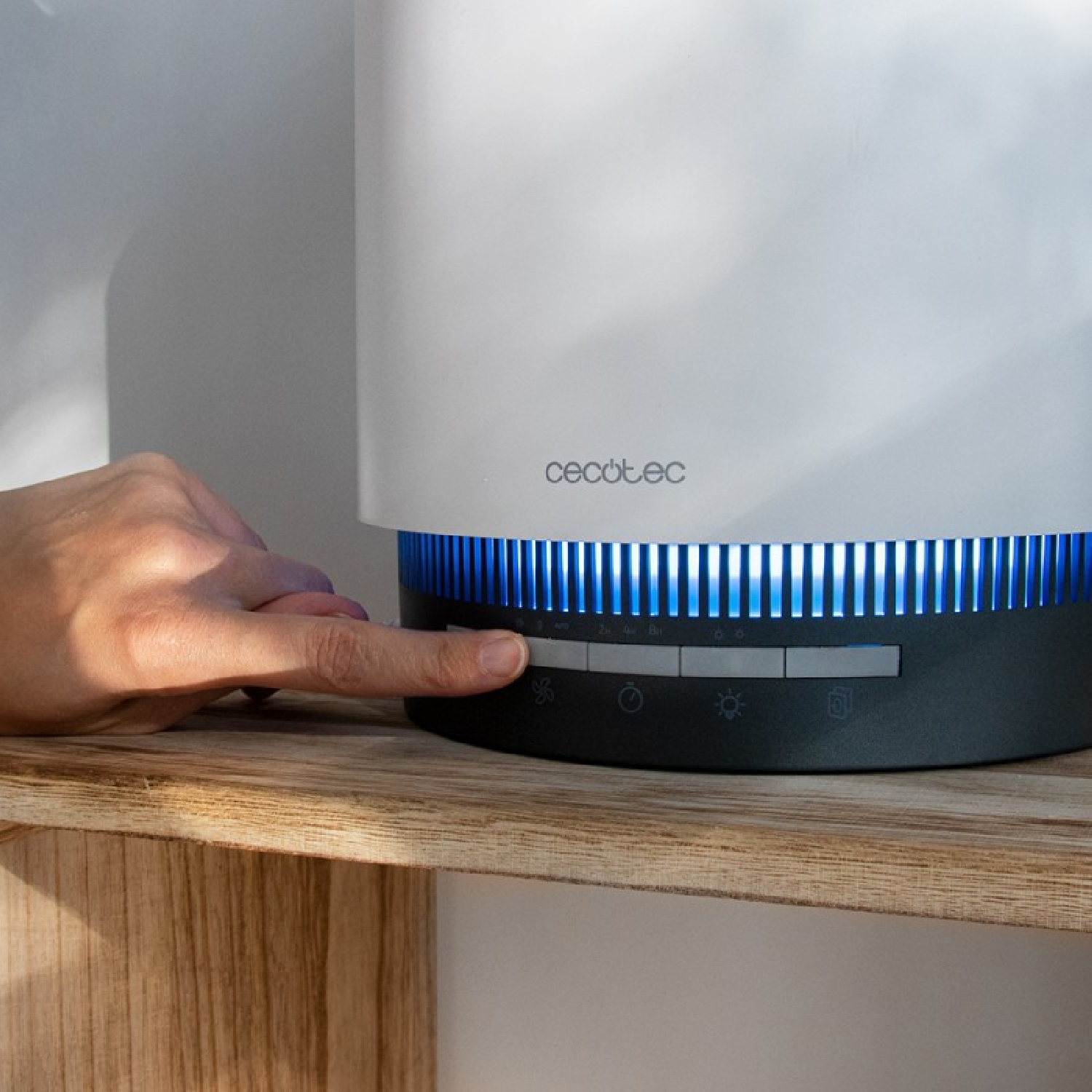 Un dito preme un pulsante su un purificatore d'aria bianco e nero con luci blu.