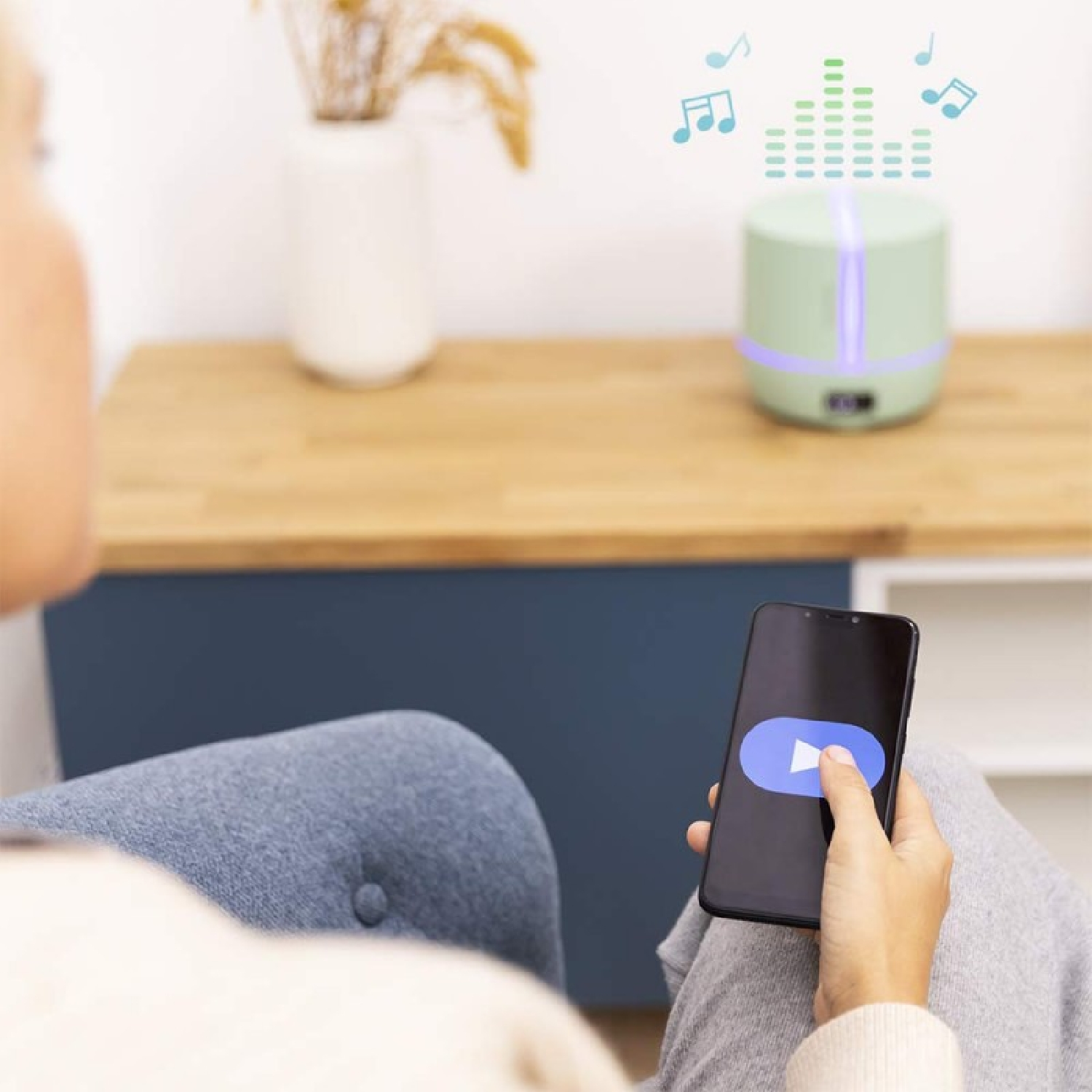 Person bedient Handy zur Steuerung eines grünen Diffusors, der Licht und Musiknoten aussendet.