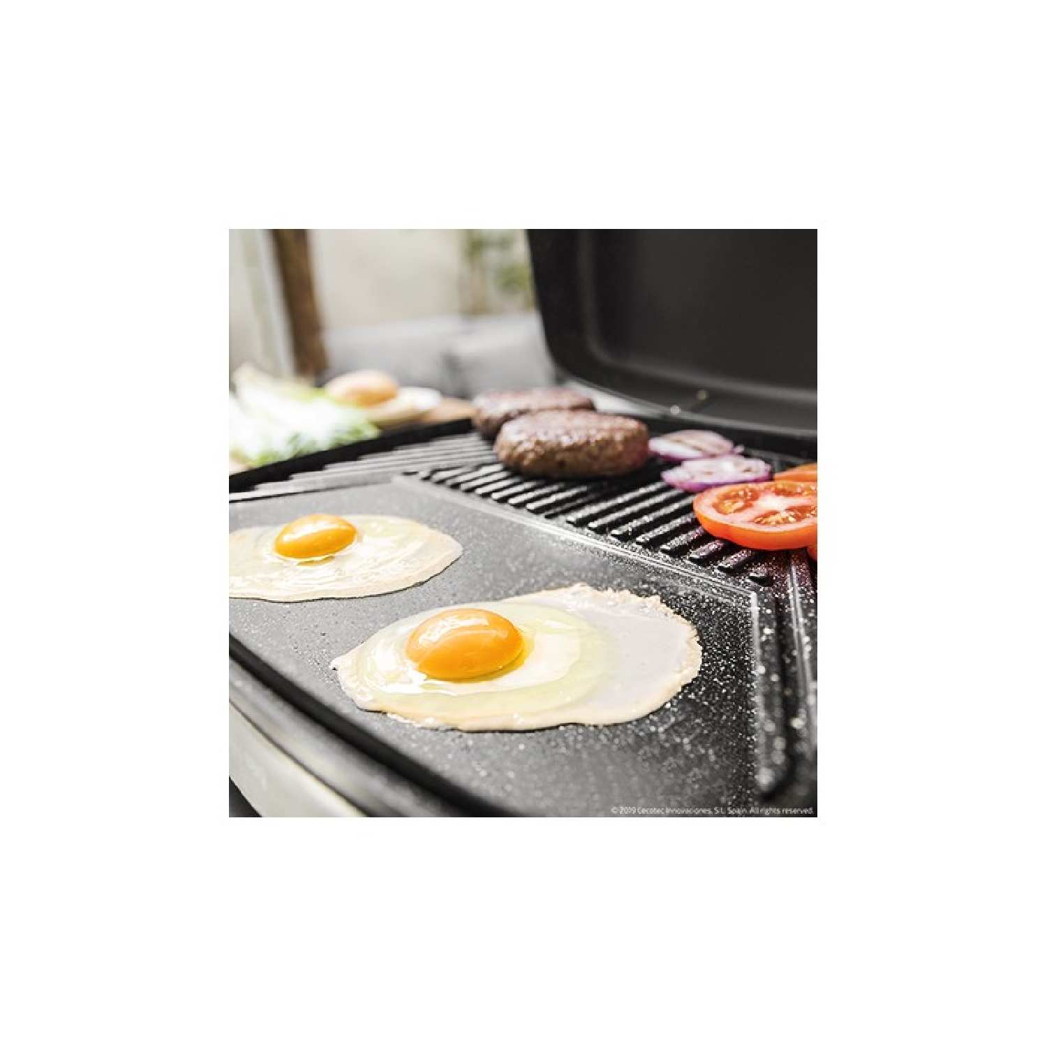 Dos huevos fritos en una plancha, con hamburguesas, cebollas y tomates cerca.