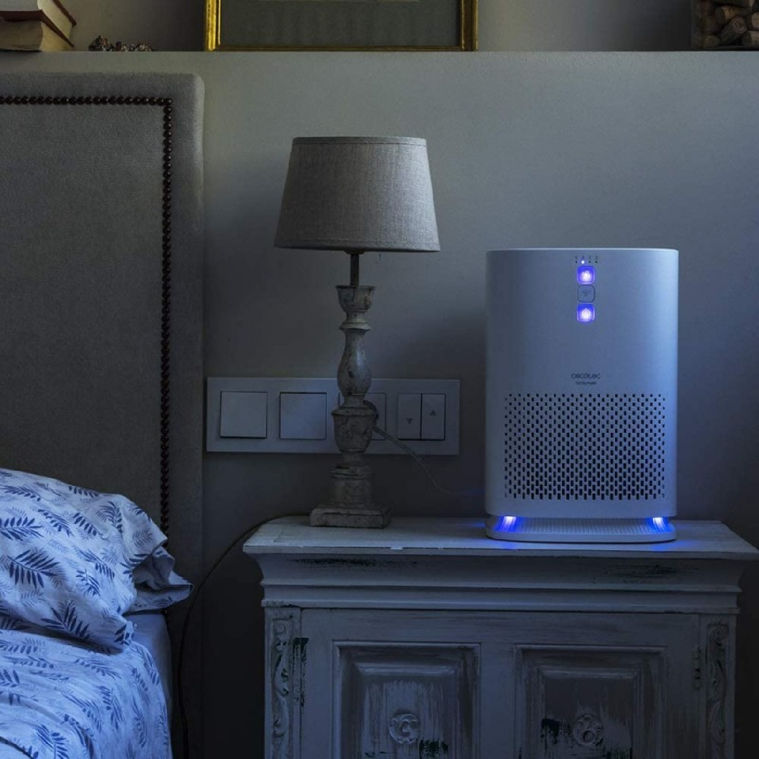 Un purificatore d'aria bianco con luci blu è su un comodino accanto a un letto.