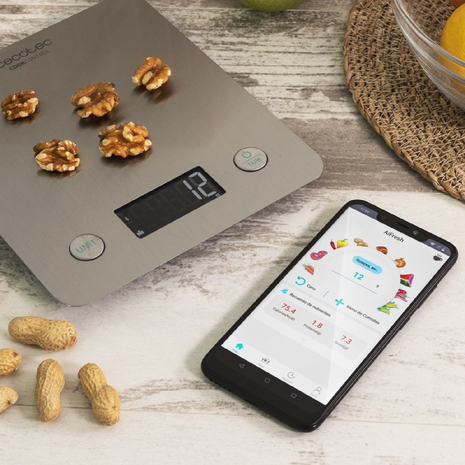 Cyfrowa waga kuchenna z orzechami włoskimi i orzeszkami ziemnymi obok, smartfon pokazuje dane o wartościach odżywczych.