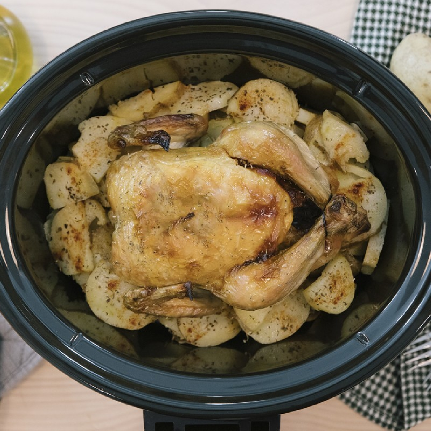 Un pollo asado con patatas en una olla de cocción lenta negra.