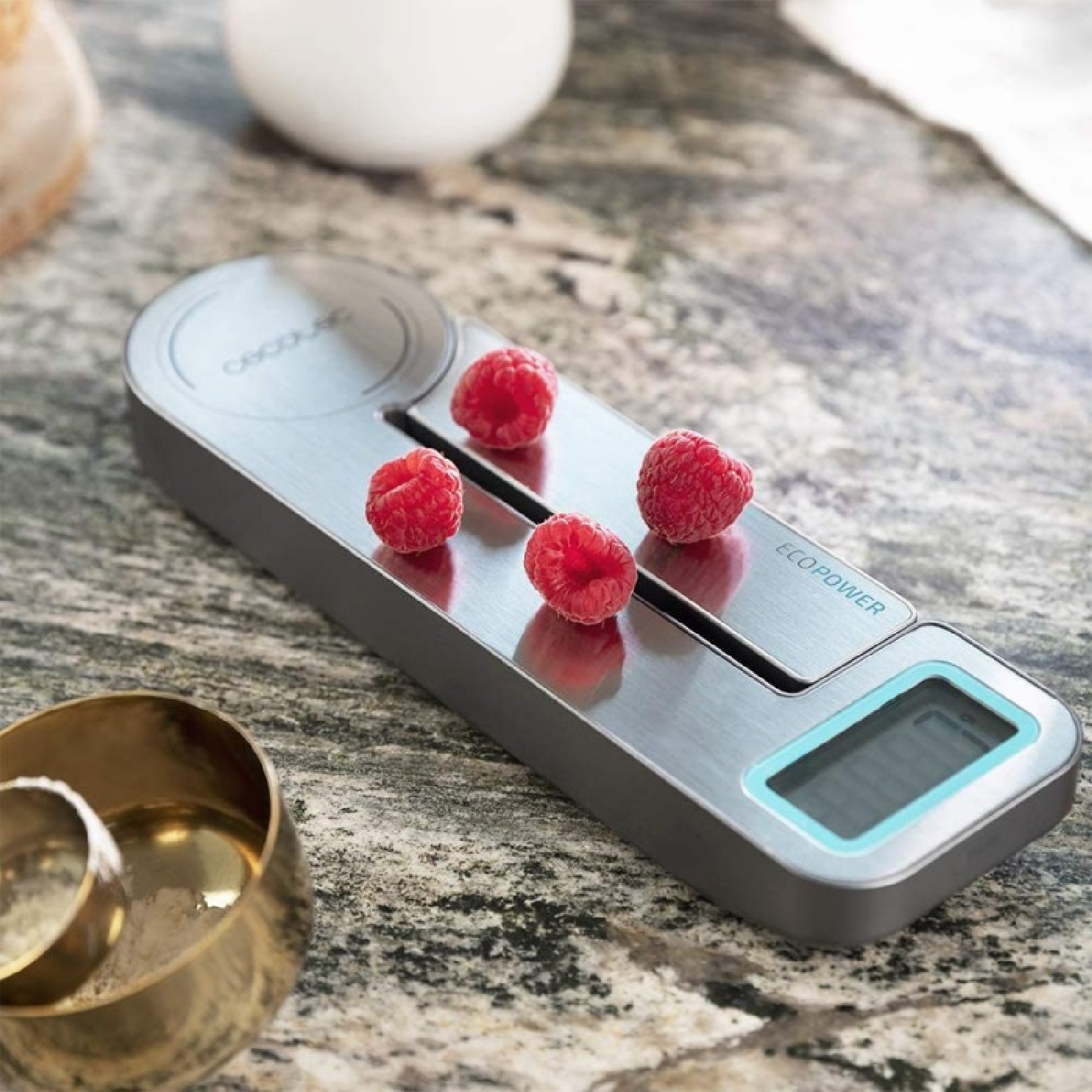 Digitale Küchenwaage mit vier Himbeeren und einer Schüssel.