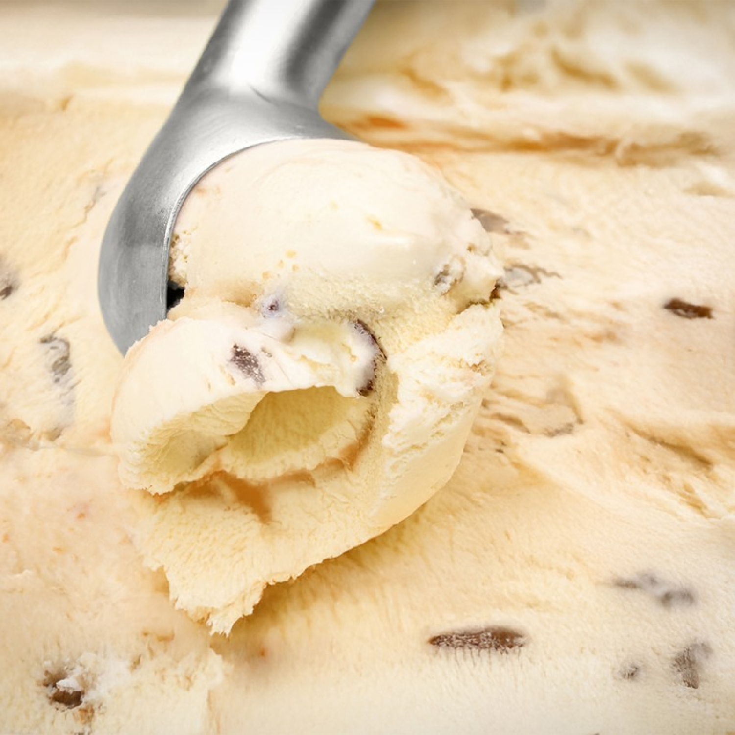 Un coppapalle solleva una pallina di gelato cremoso, giallo chiaro con pezzi scuri da una porzione più grande.