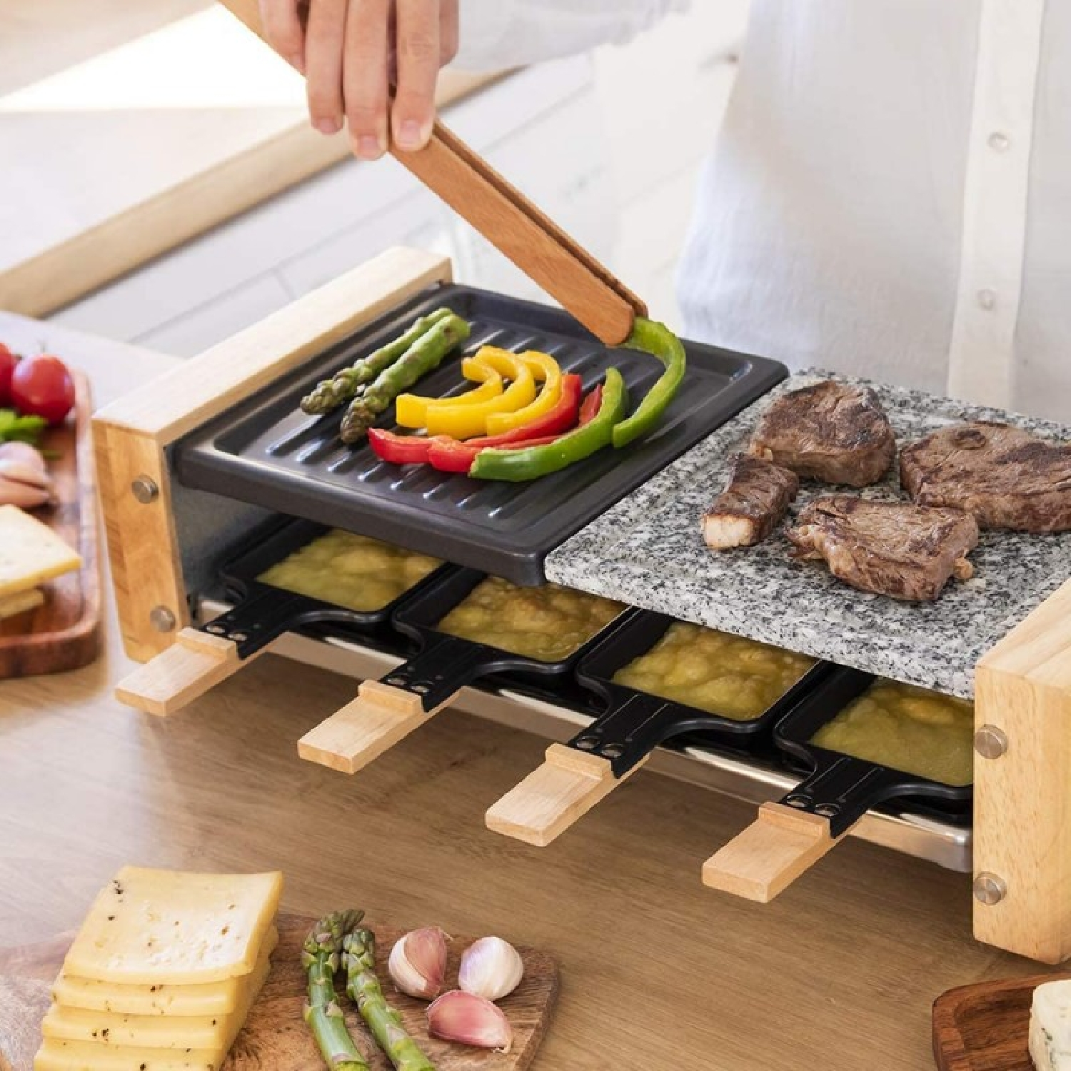 Grill do raclette z mięsem, warzywami i serem na drewnianym stole.