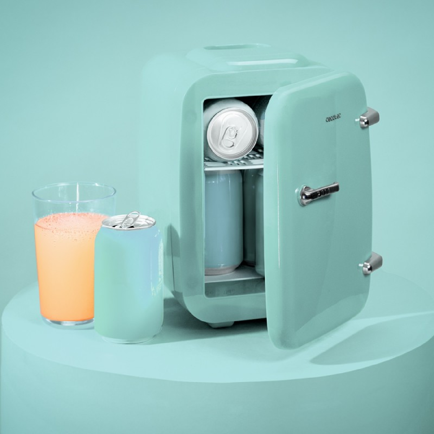 Un mininevera verde menta con la puerta abierta, que contiene latas y un vaso de bebida naranja.