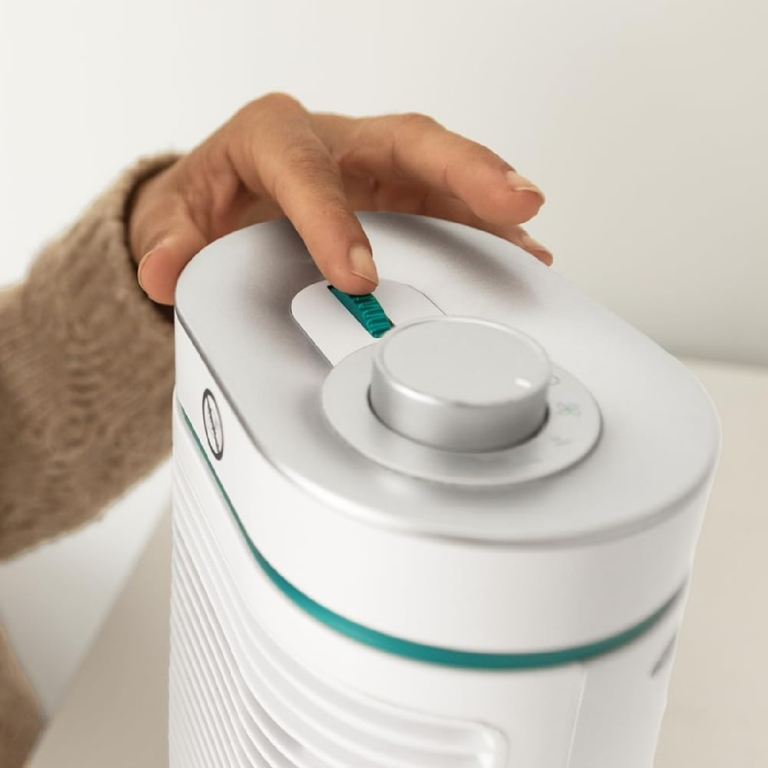 Een hand stelt de knop van een witte ventilator met een turquoise accentstreep af.