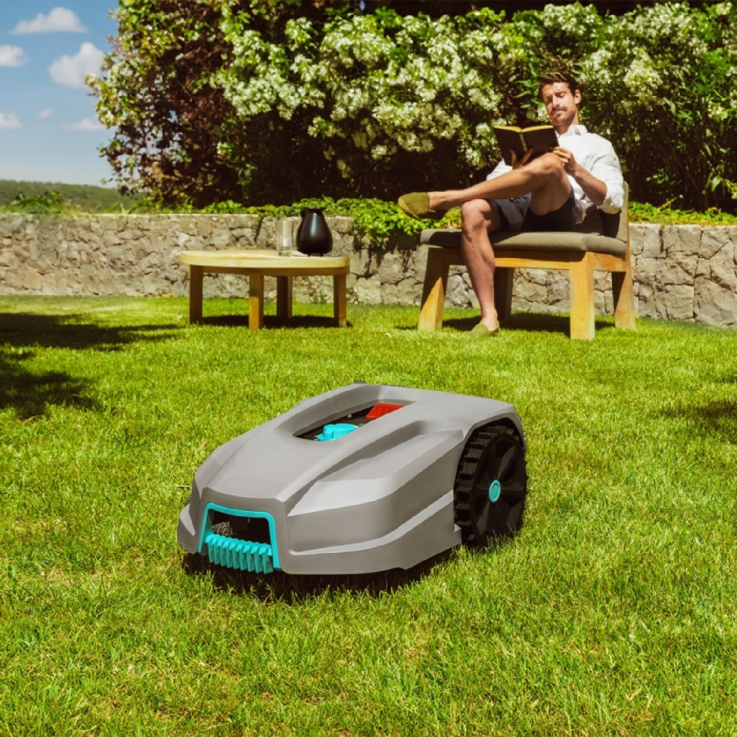 Robot koszący trawę stoi na trawie, mężczyzna czyta w tle.