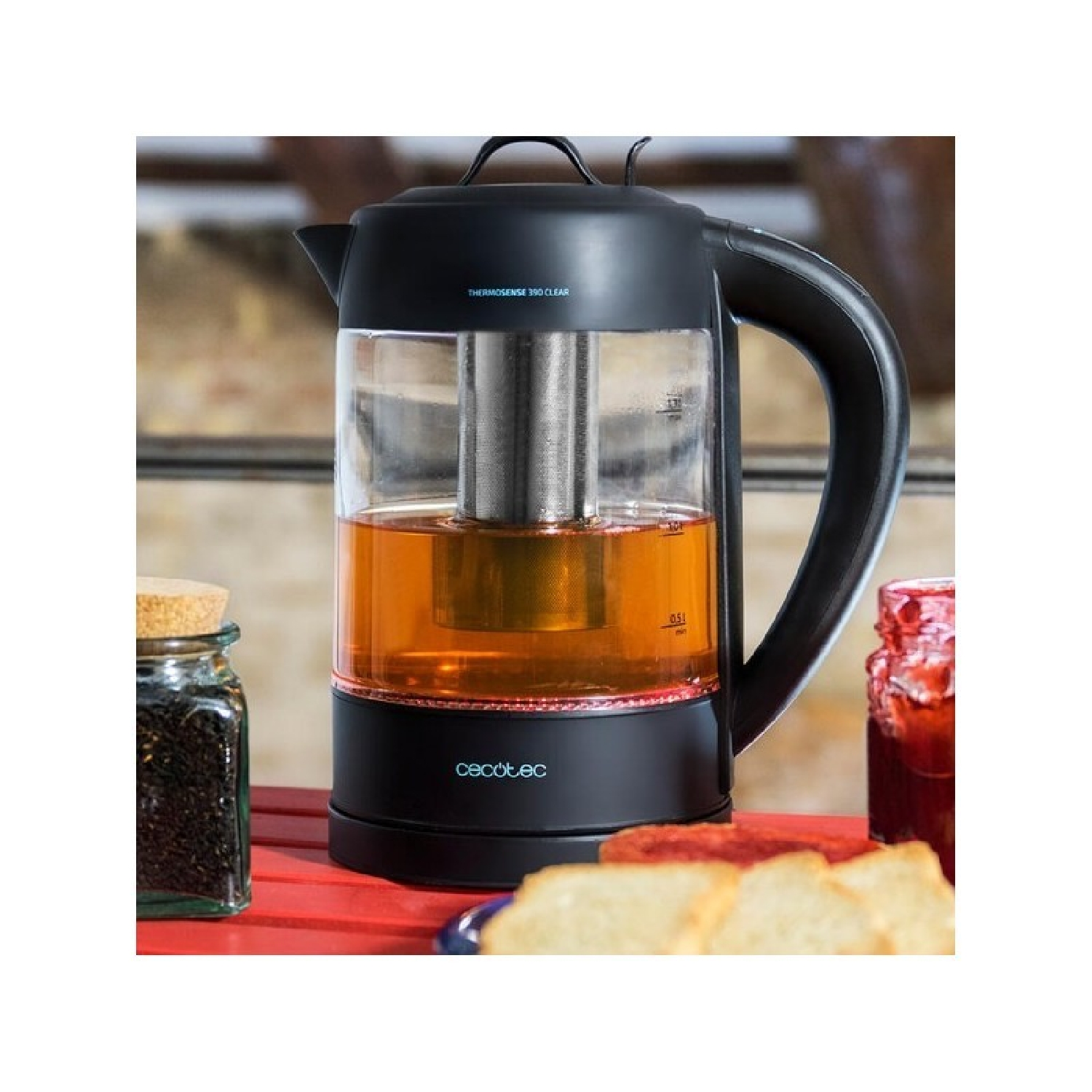 Tetera negra con cuerpo de vidrio, llena de té, junto a mermelada y tostadas.