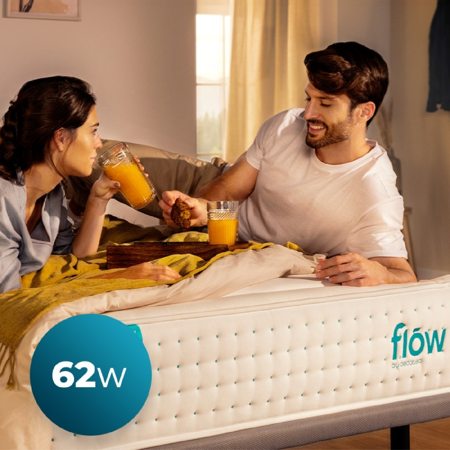 Coppia a letto a colazione. Donna beve succo, uomo mangia dolce. Materasso mostrato.