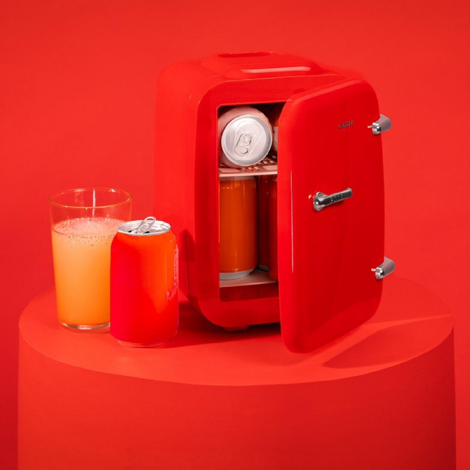 Un mininevera rojo con puerta abierta, lleno de latas. Al lado hay un vaso y una lata.