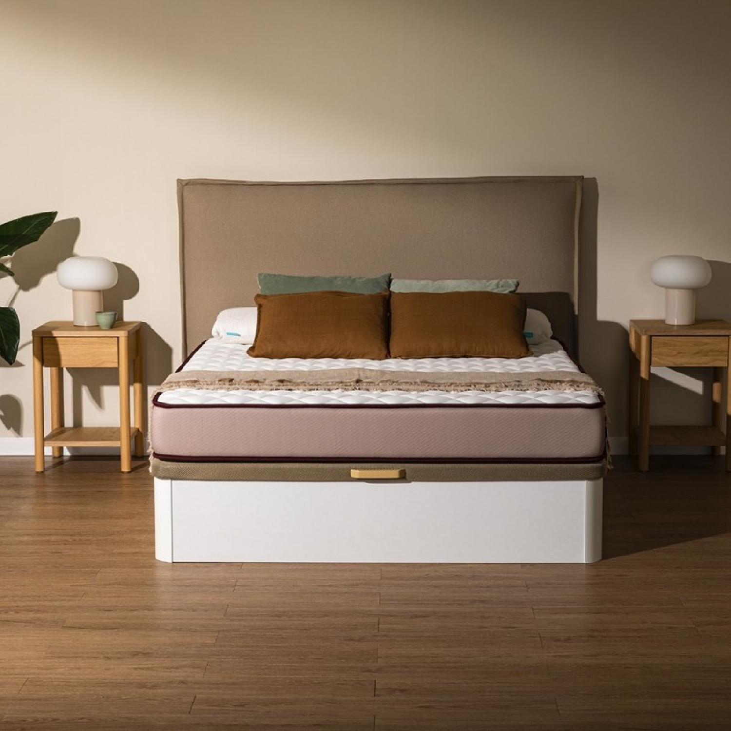 Een bed met een beige hoofdbord, bruine en groene kussens, en een roze matras op een witte basis.