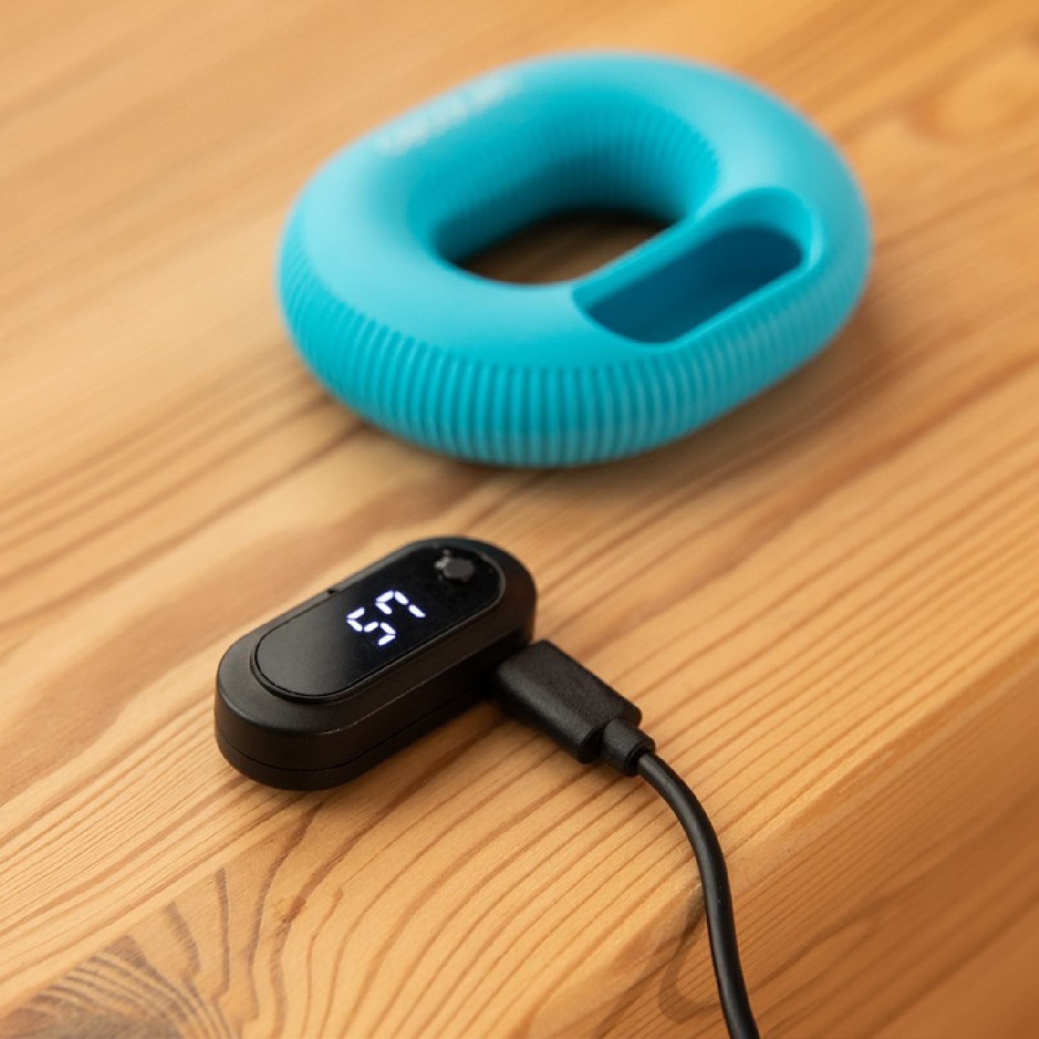 Un ejercitador de agarre azul descansa sobre una mesa de madera junto a un contador digital negro.