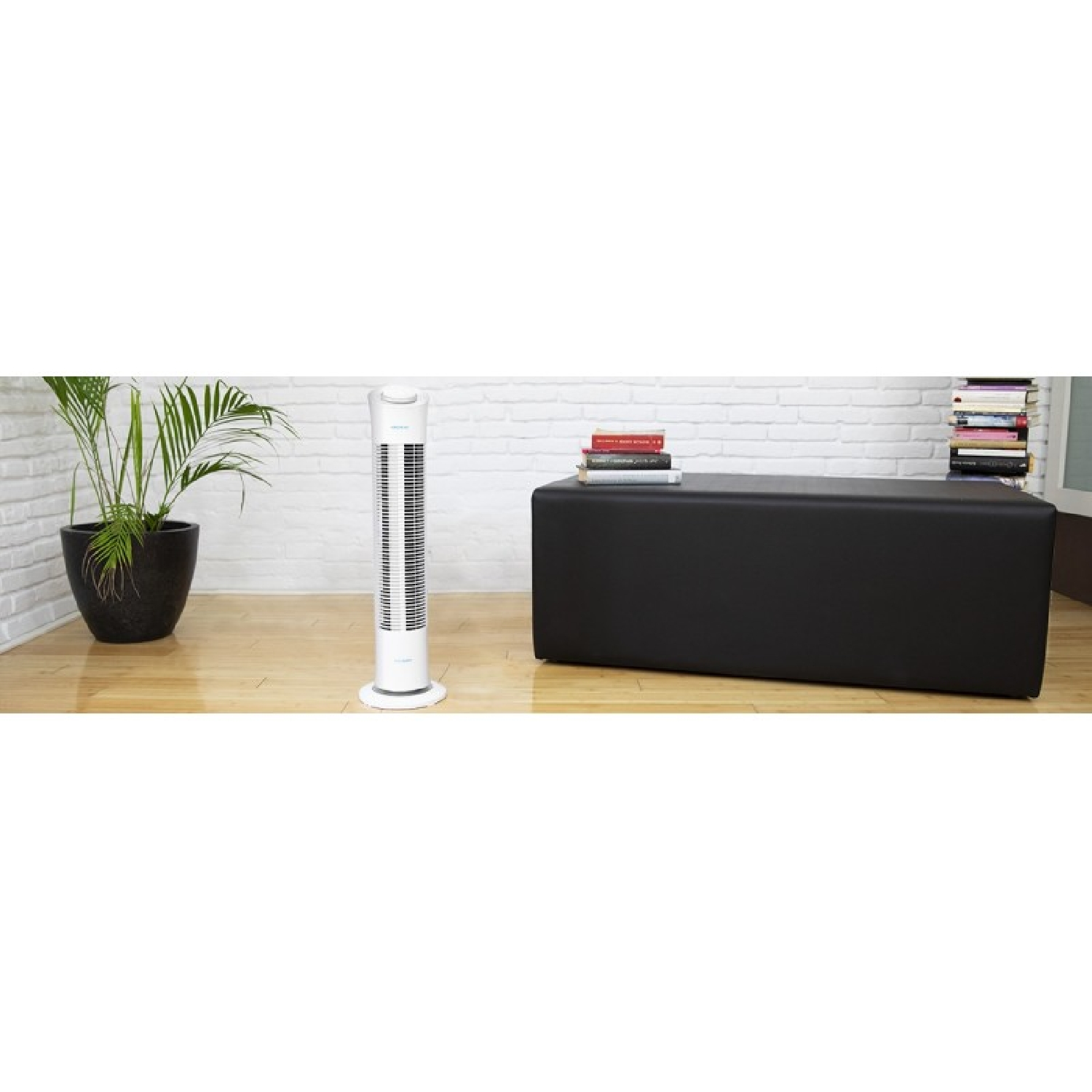 A slim white tower fan stands next to a black ottoman with books.