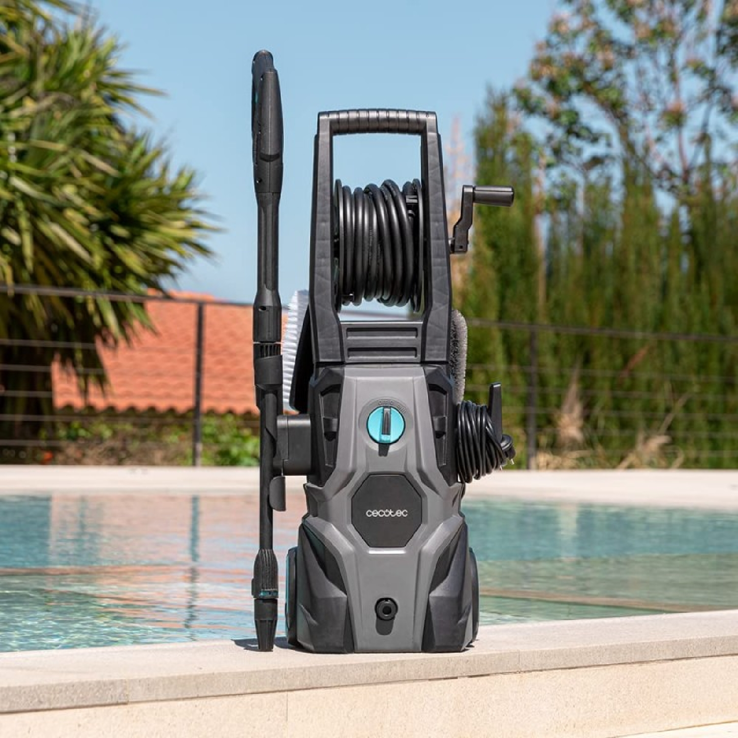 Un'idropulitrice grigia con tubo e lancia a spruzzo si trova vicino a una piscina.