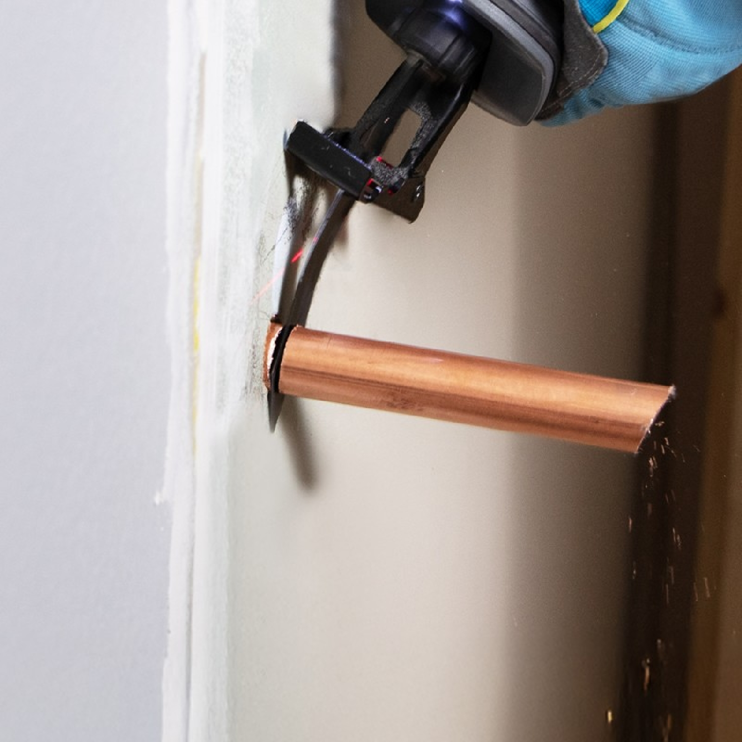 Una mano enguantada usa una sierra recíproca para cortar un tubo de cobre que sobresale de una pared.
