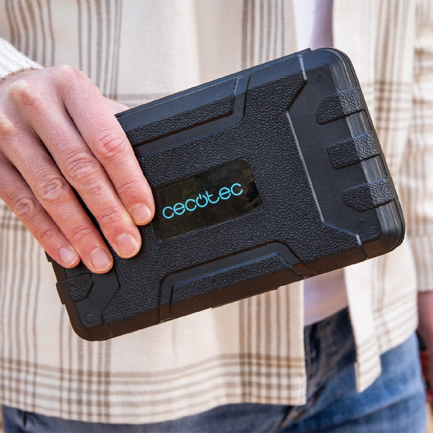 Una mano tiene un power bank nero e robusto con logo blu Cecotec.
