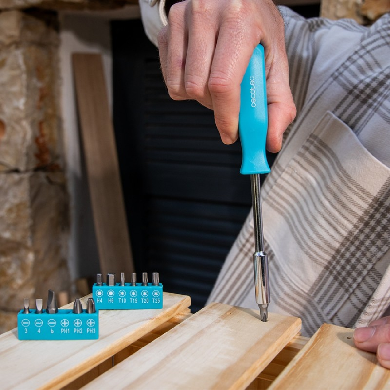Una mano usa un cacciavite blu per avvitare legno. Set di punte sono vicini.