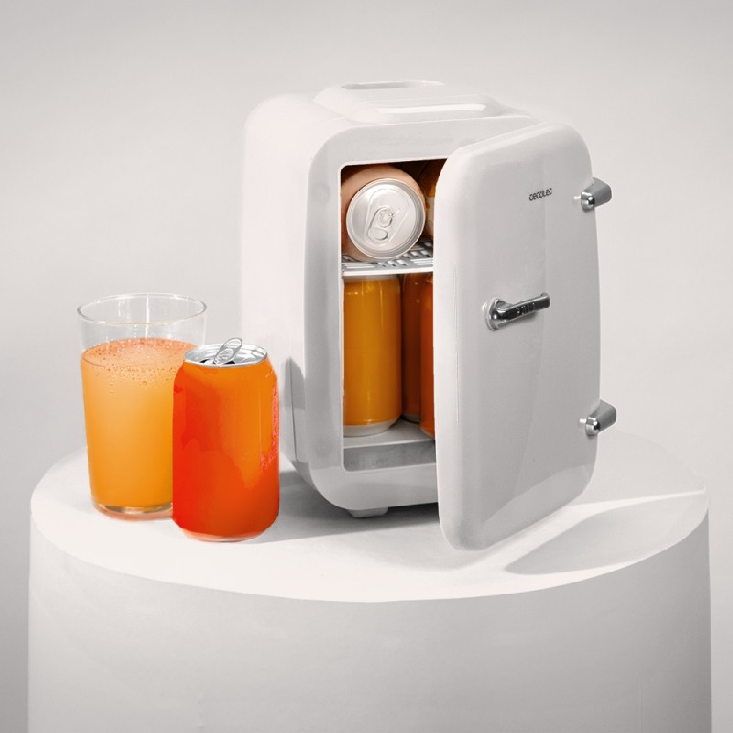 Pequeña nevera blanca con puerta abierta, vaso y lata de bebida de naranja al lado.