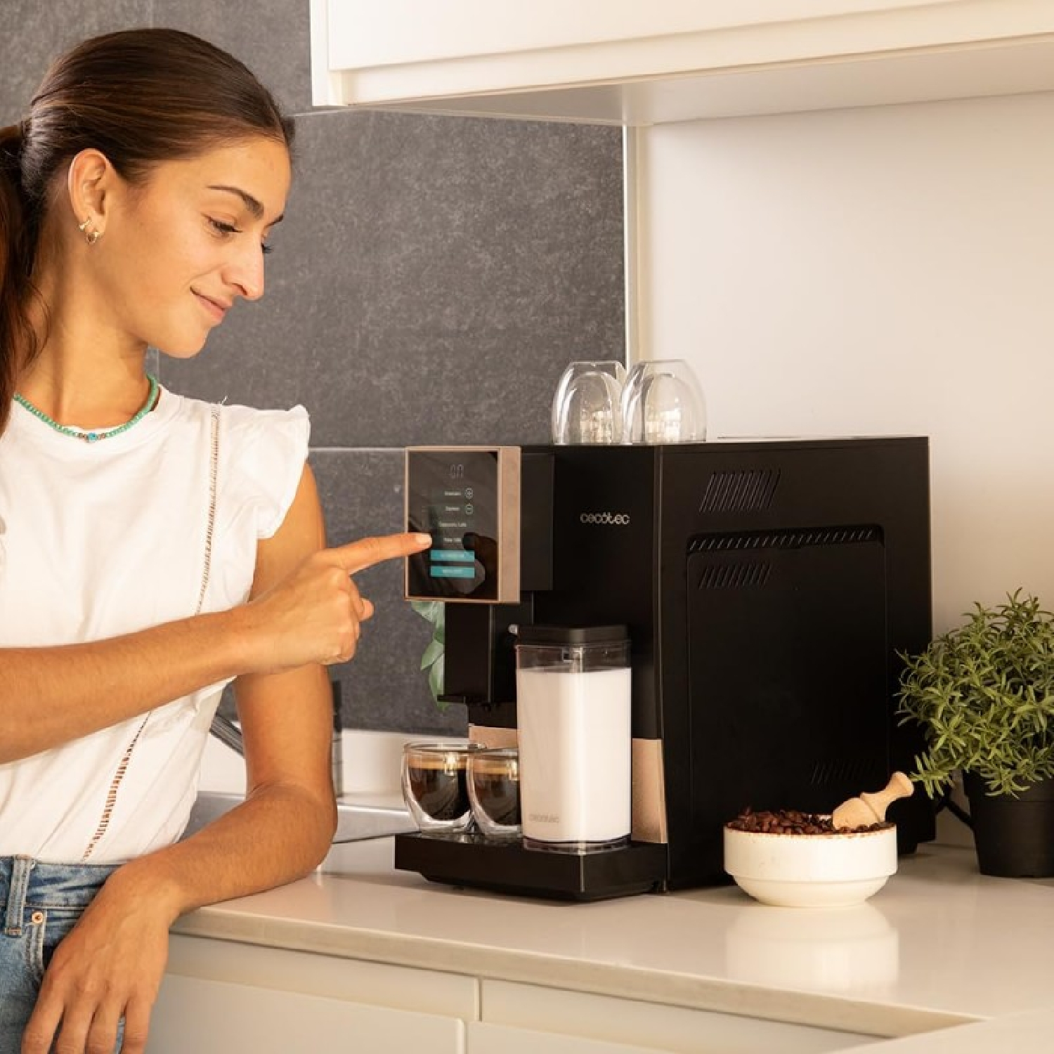 Donna usa macchina da caffè con touchscreen, tazze e chicchi nelle vicinanze.