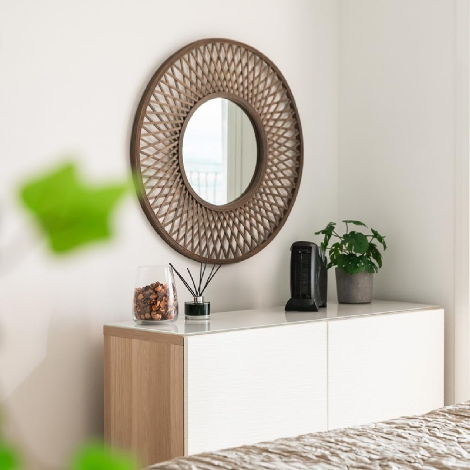 Uno specchio rotondo con cornice in legno è appeso sopra una cassettiera bianca con decorazioni.