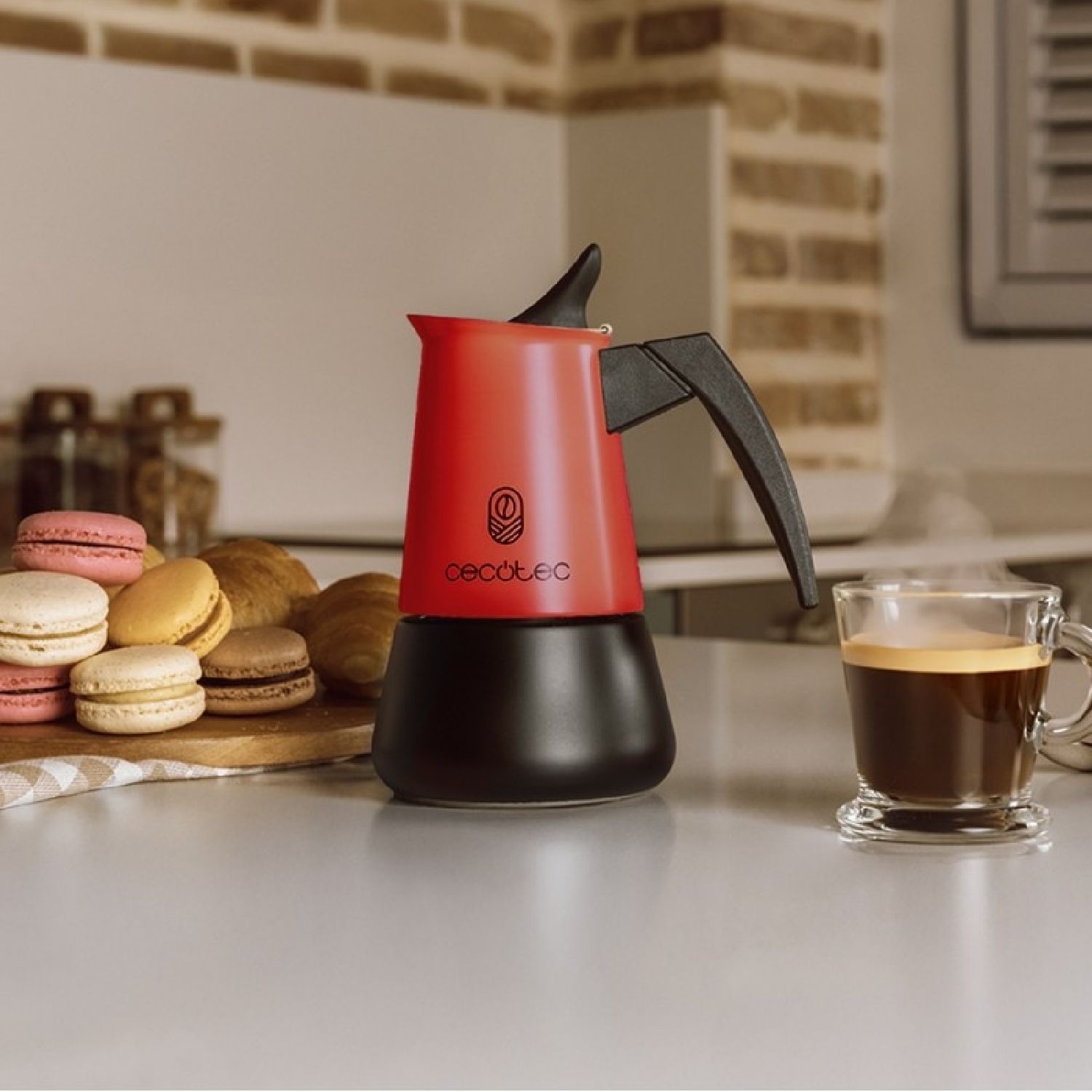 Eine rote Kaffeemaschine steht neben einem Glas Espresso. Macarons und Gebäck liegen daneben.