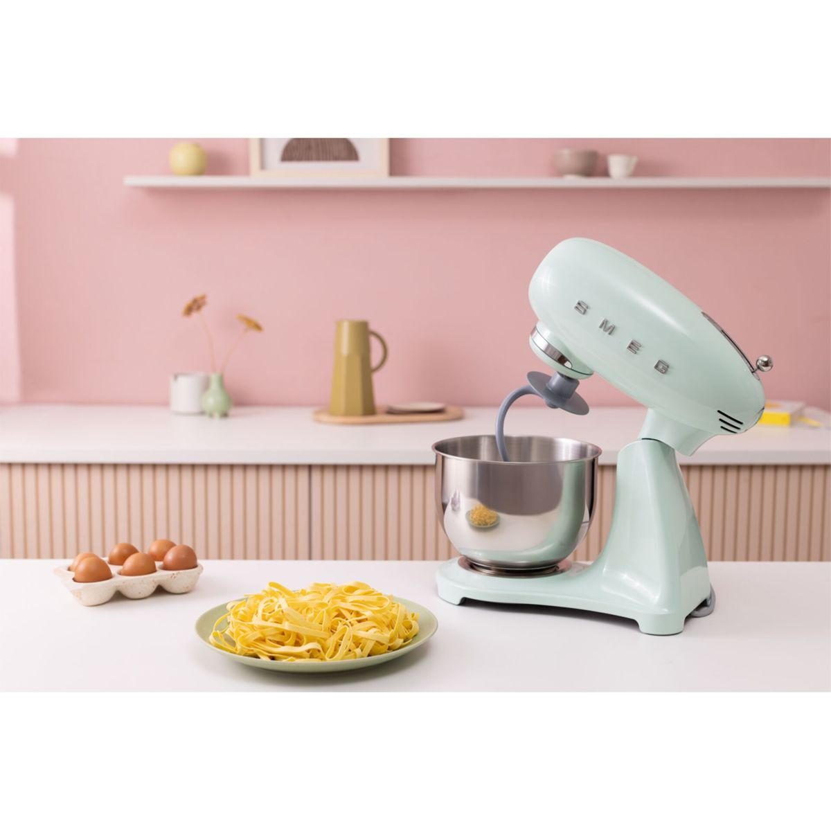Un robot de cocina Smeg verde claro junto a un tazón de pasta y huevos.
