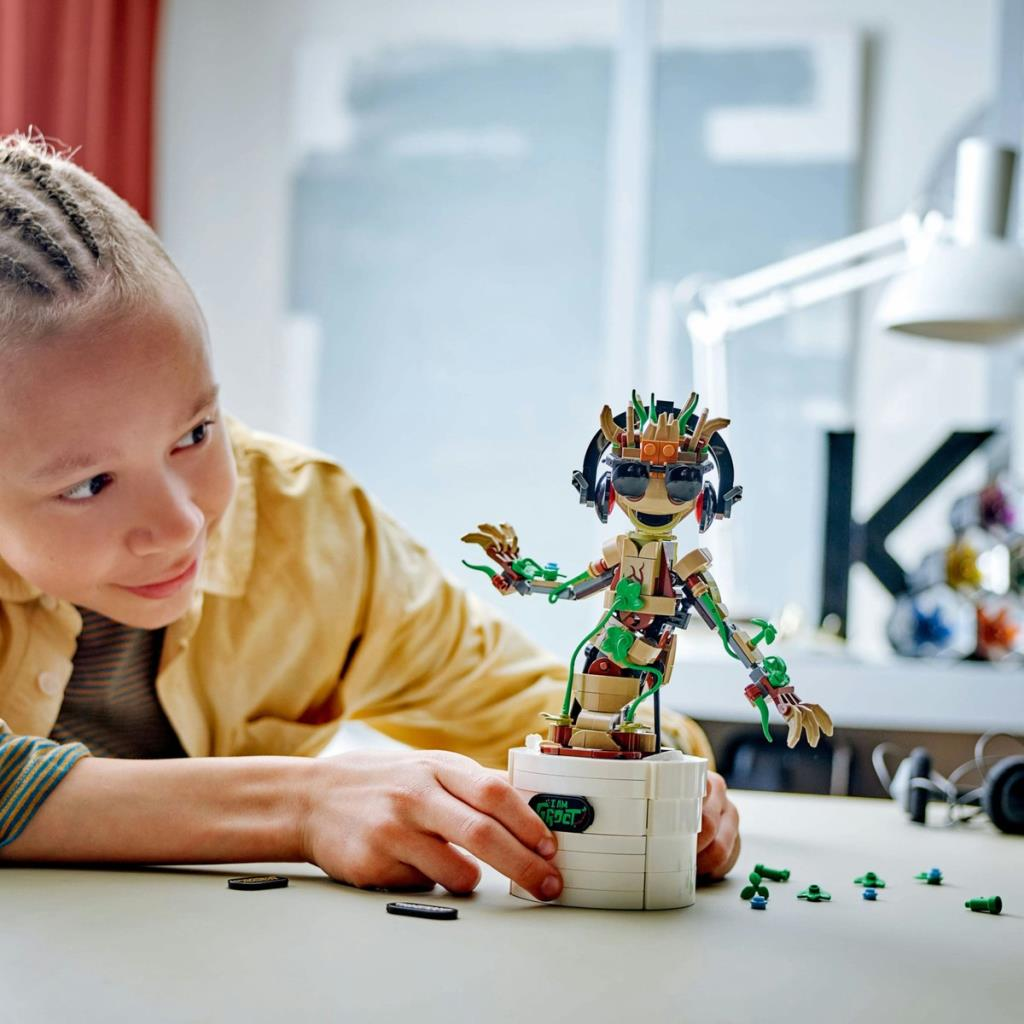 Bir çocuk masada kulaklıklı ve güneş gözlüklü bir LEGO Groot inşa ediyor.