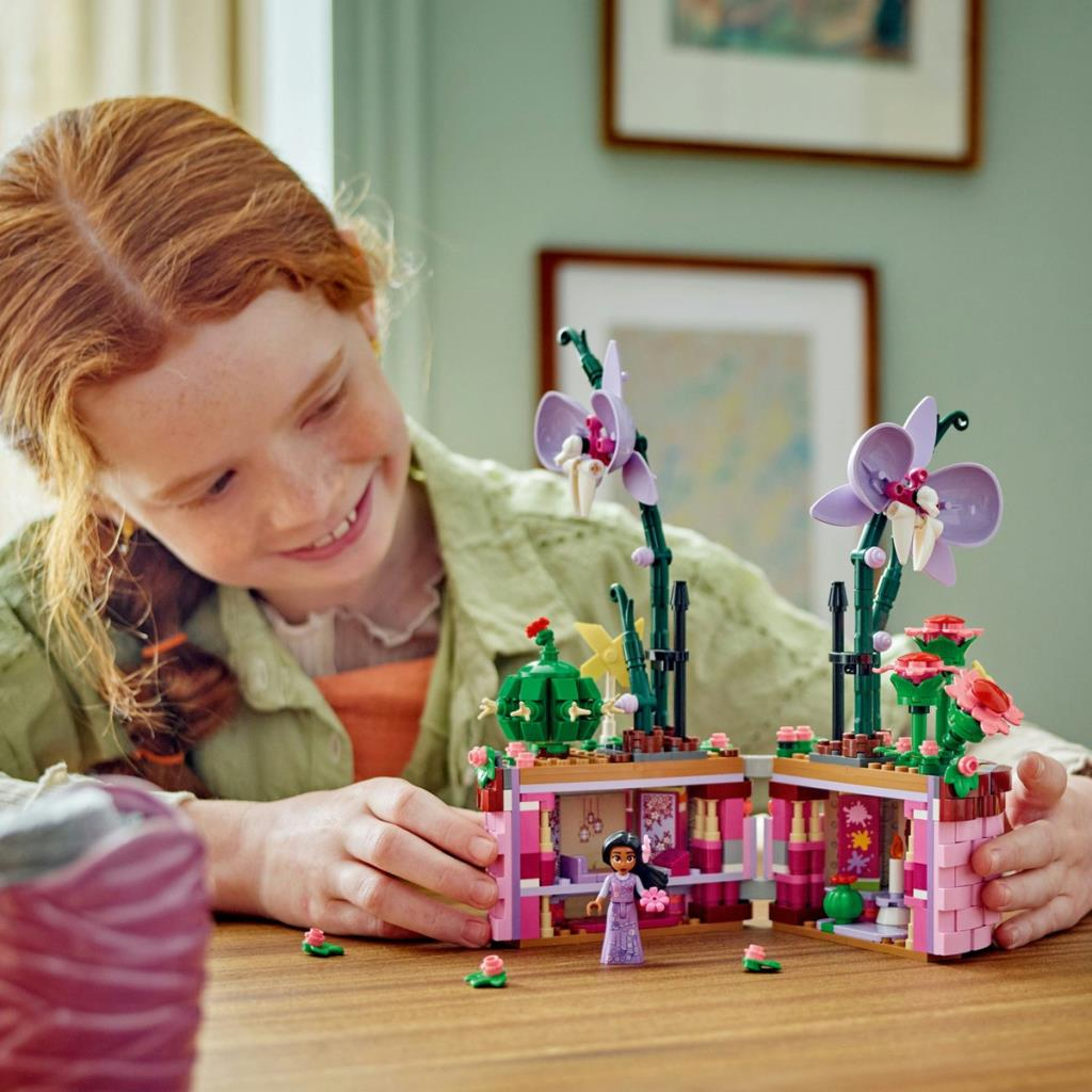 Una niña construye una casa de flores de Lego con una figura y orquídeas moradas.