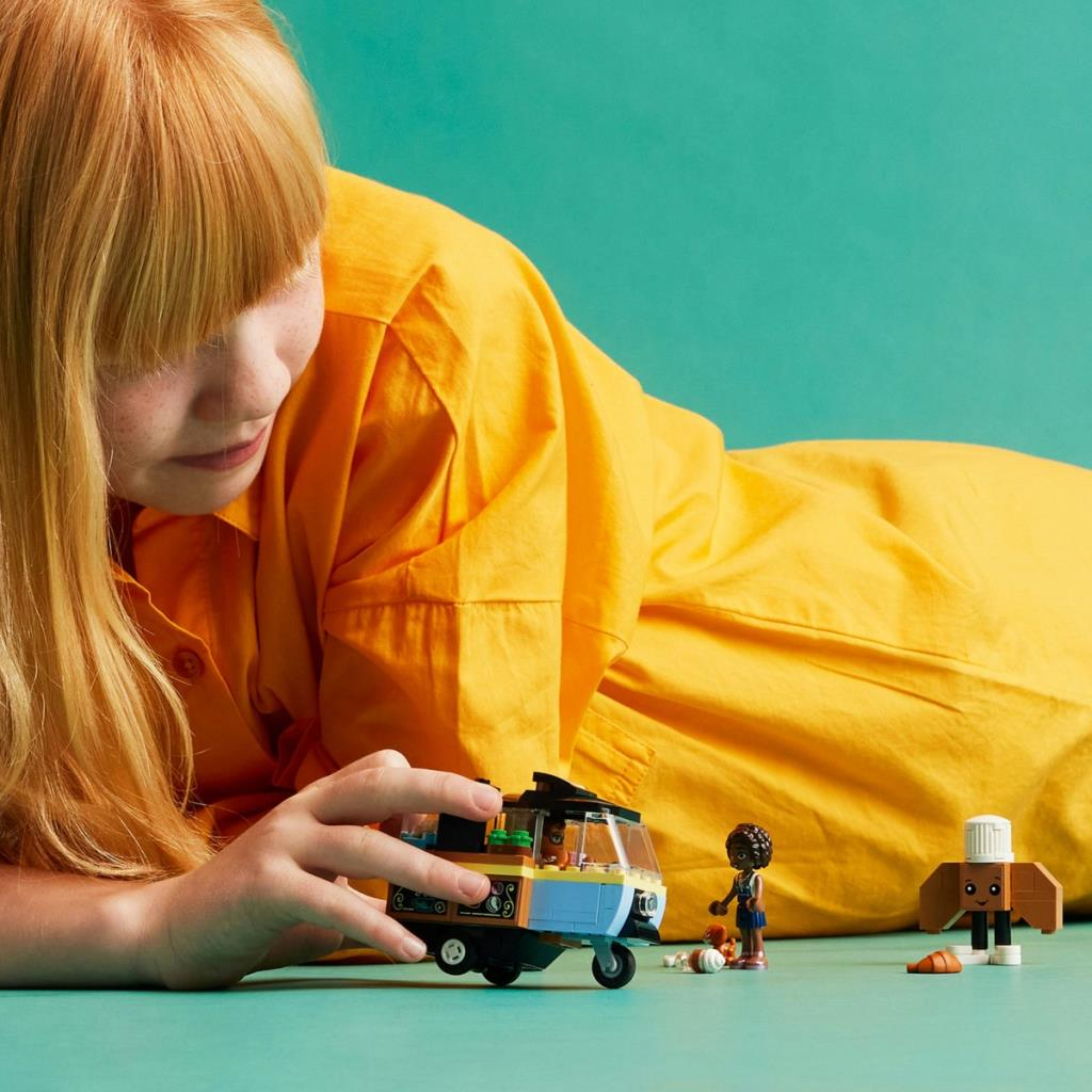 Kızıl saçlı bir kız, Lego figürleri ve mavi-sarı bir araçla oynuyor.