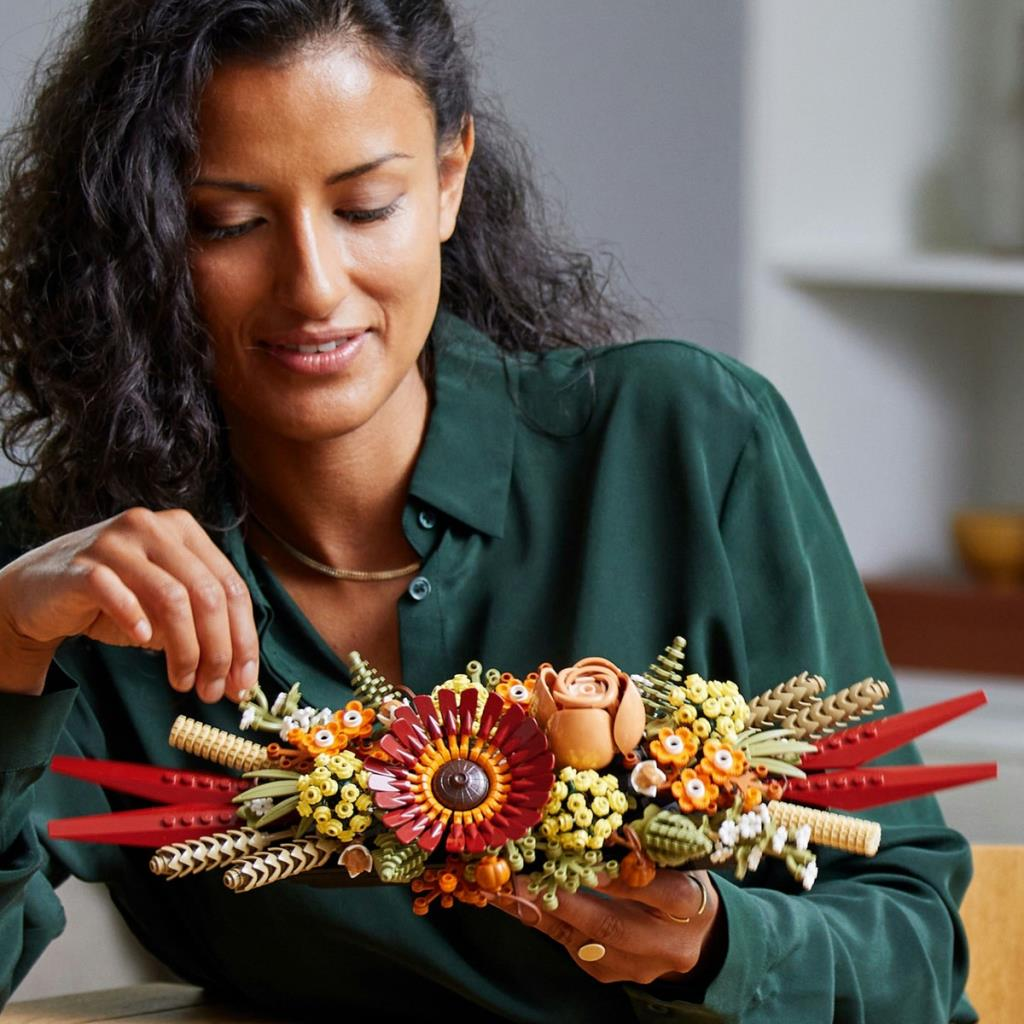 Une femme aux cheveux foncés tient un bouquet de fleurs colorées en LEGO.