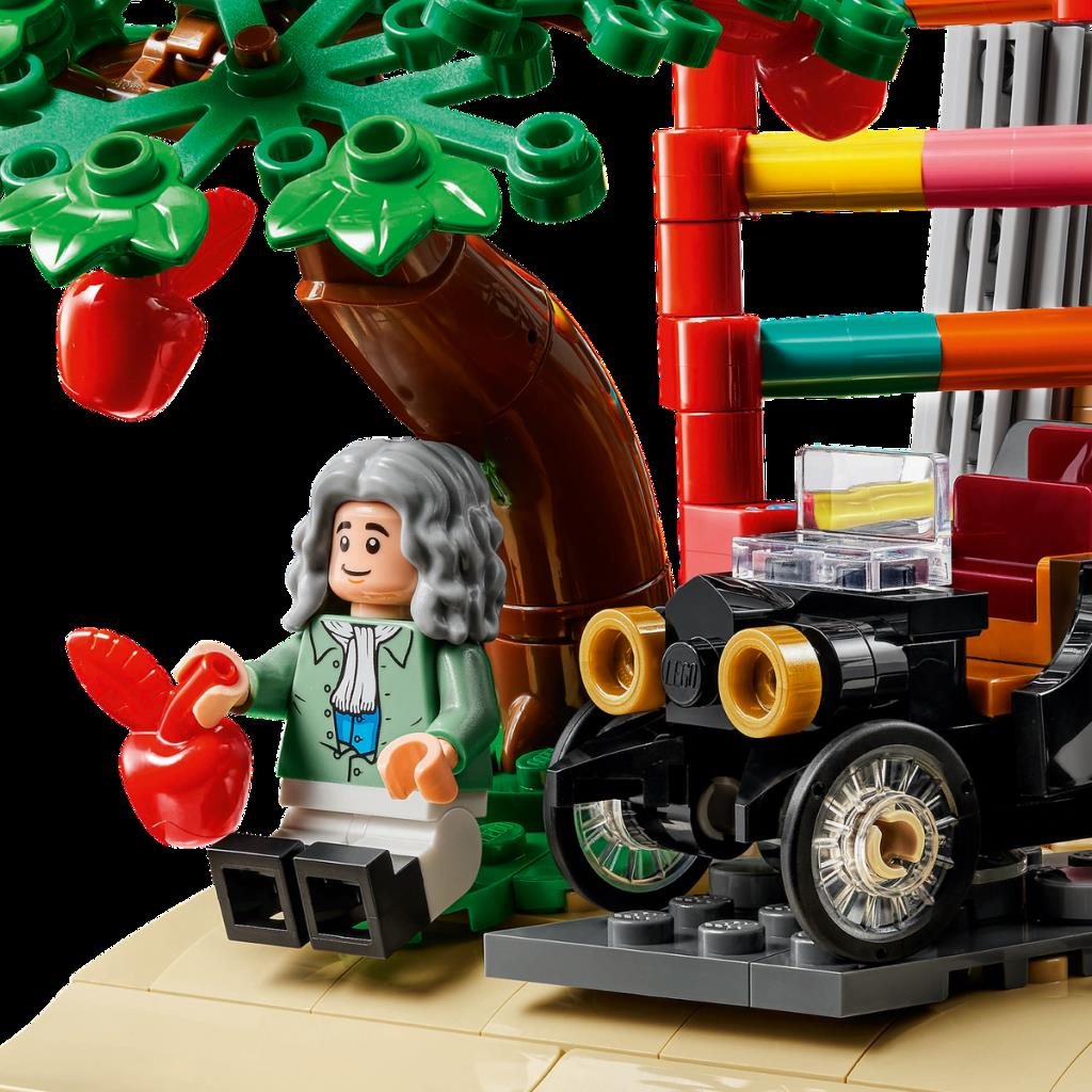 Bir Lego Newton figürü elmalı bir ağacın altında, bir arabanın yanında oturuyor.