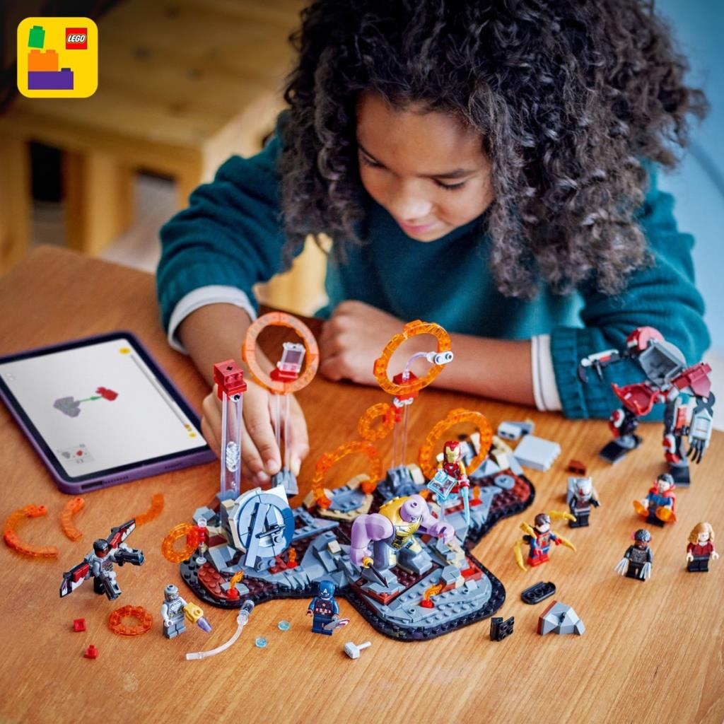 Çocuk ahşap masada süper kahraman figürleri ve Thanos ile Lego seti yapıyor.