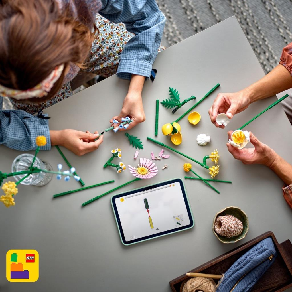 Eller talimatları gösteren bir tabletle masada Lego çiçekleri monte ediyor.