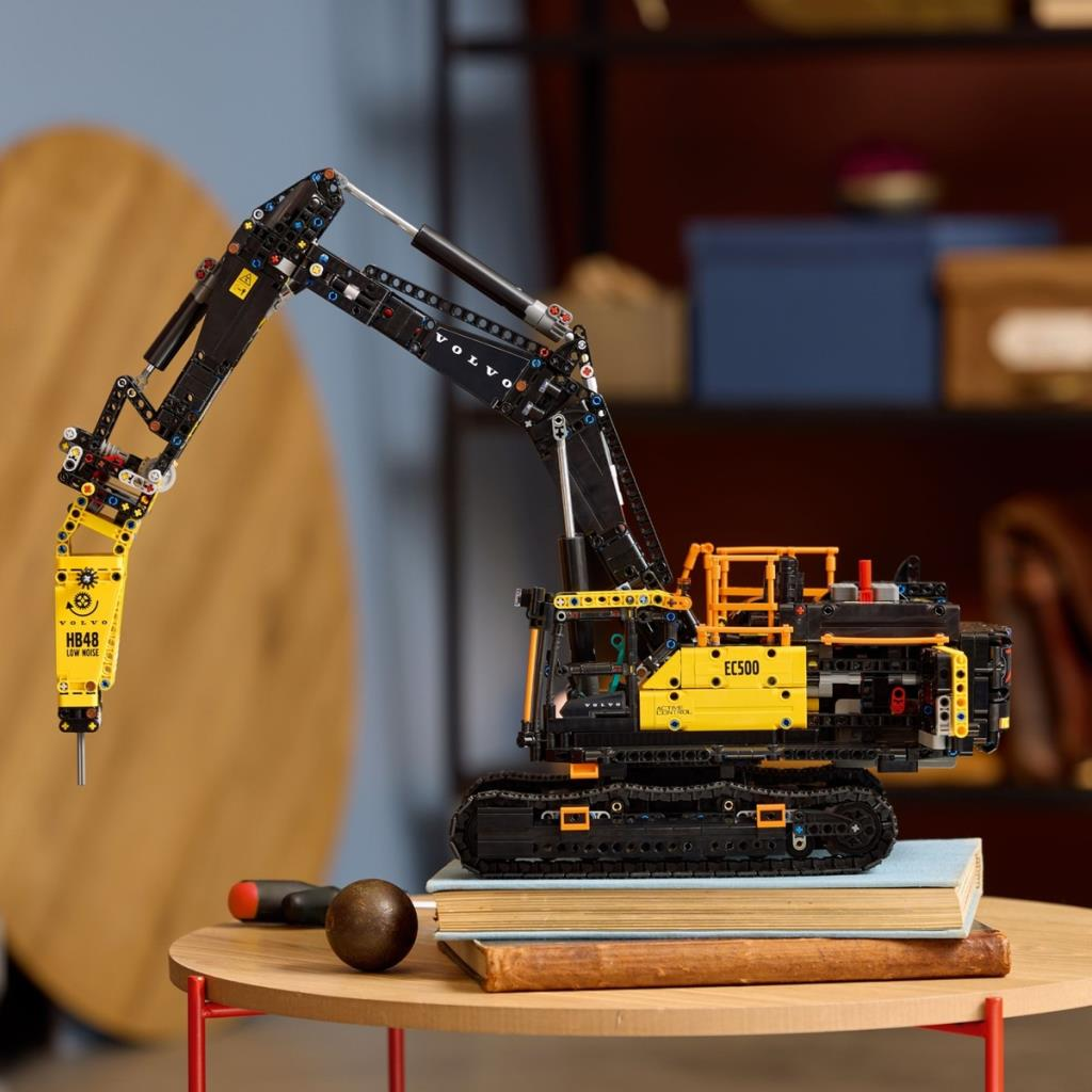 Sarı ve siyah paletli Lego ekskavatör kitapların üzerinde duruyor.