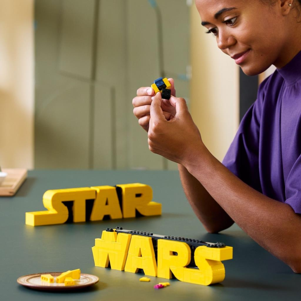 Kadın sarı LEGO Star Wars harfleri inşa ediyor. Küçük bloklar tutuyor.