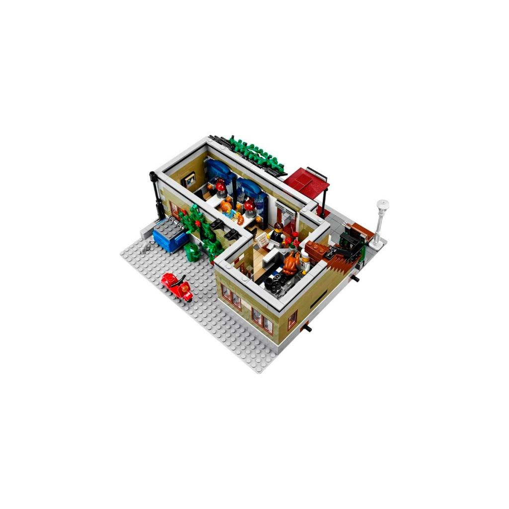 Lego gebouw met rode auto, figuren en bomen.