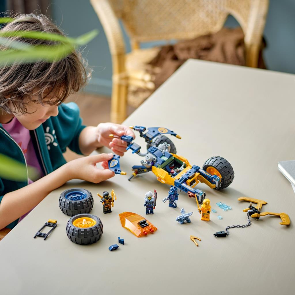 Bir çocuk masanın üzerinde figürler ve tekerleklerle sarı ve mavi Lego motosiklet yapıyor.